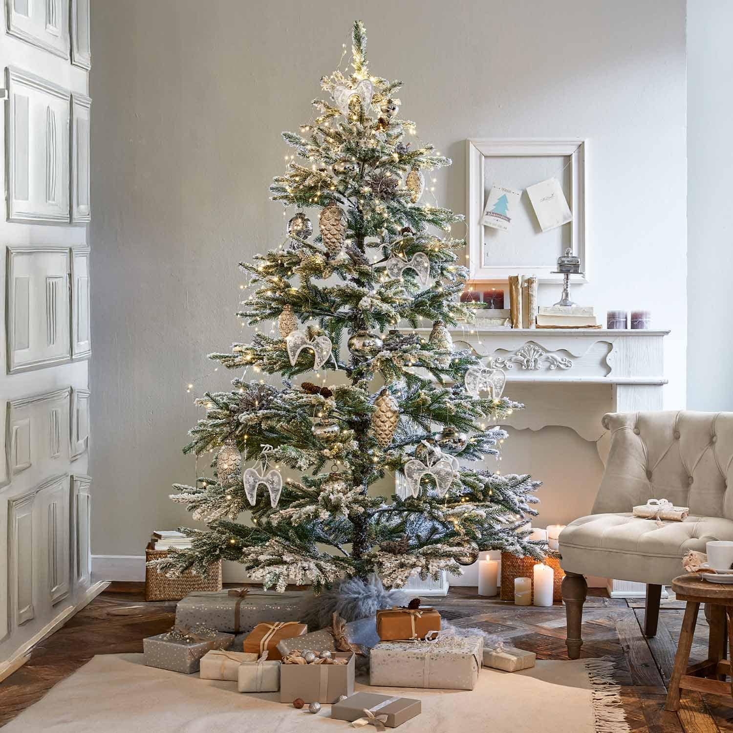 Sapin de Noël enneigé décoré d'anges blancs et de pommes de pin dorées avec cadeaux au pied dans un salon cosy