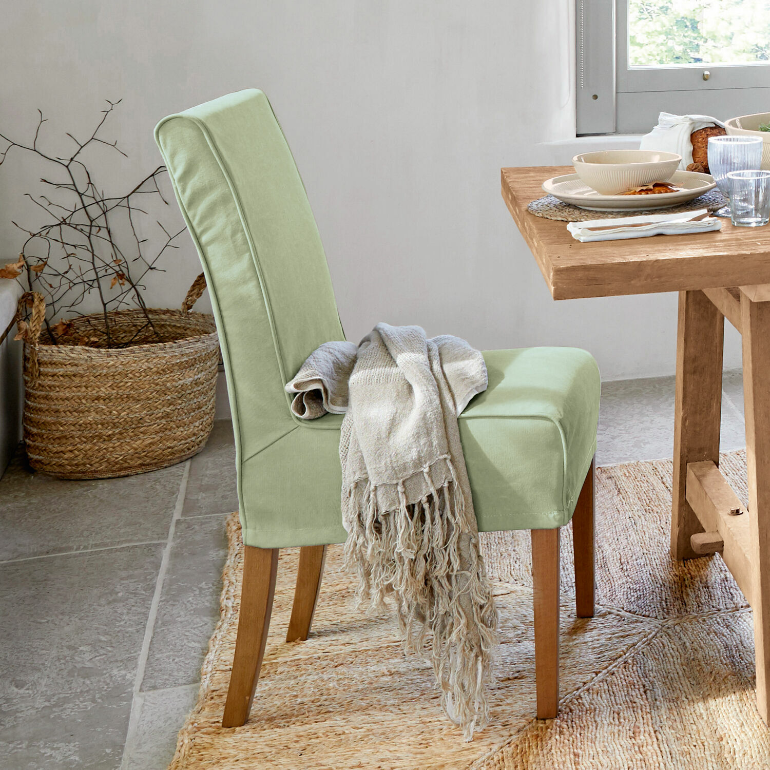 Chaise rembourrée vert clair avec pieds en bois et plaid beige dans une salle à manger lumineuse