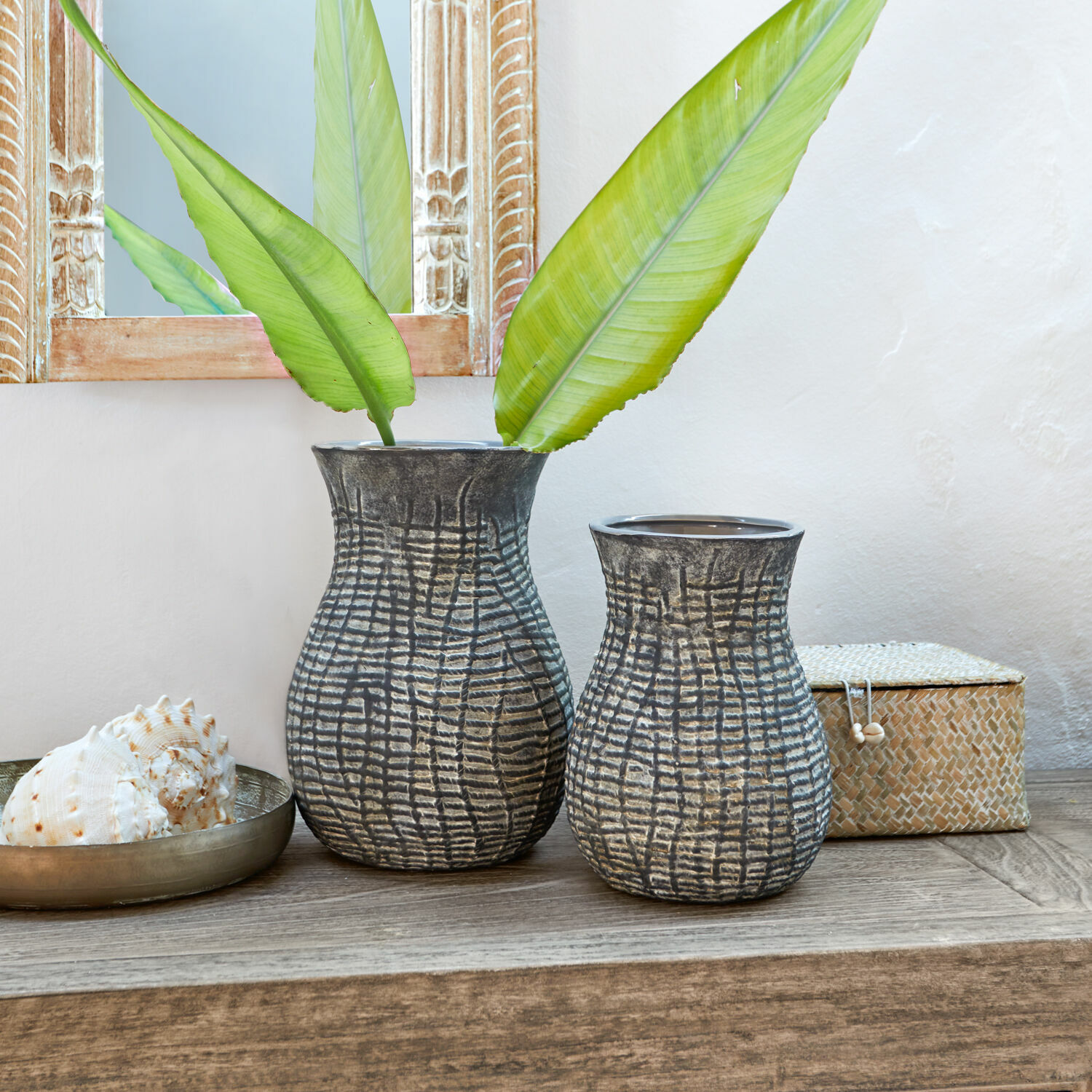 Lot de 2 vases Fahrid Deux vases en céramique gris foncé avec motif texturé posés sur une table en bois avec des feuilles vertes