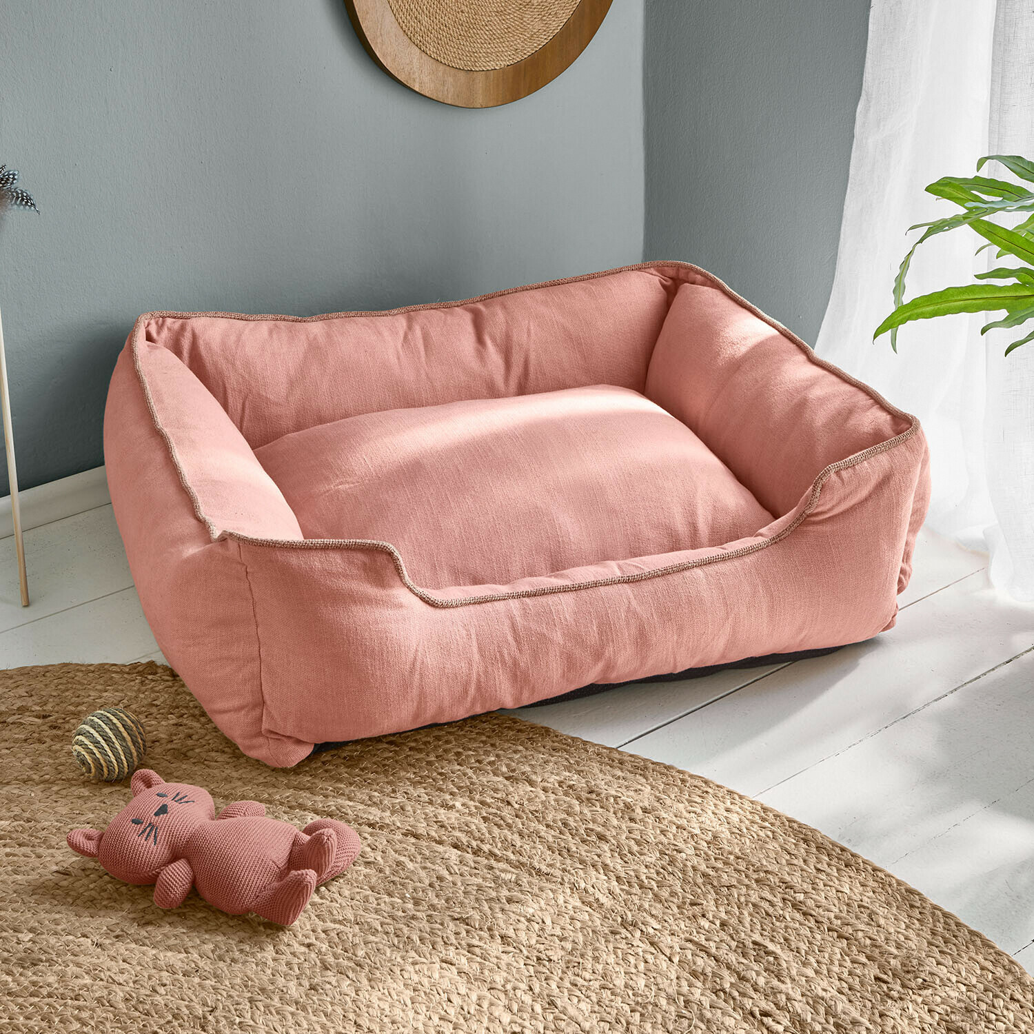 Panier pour chien rose en tissu doux sur sol clair avec jouet chat et balle en corde