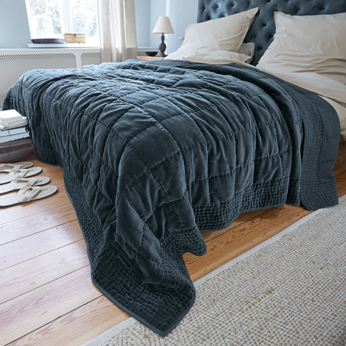 Plaid matelassé gris foncé en tissu doux sur lit dans une chambre lumineuse, décoration intérieure