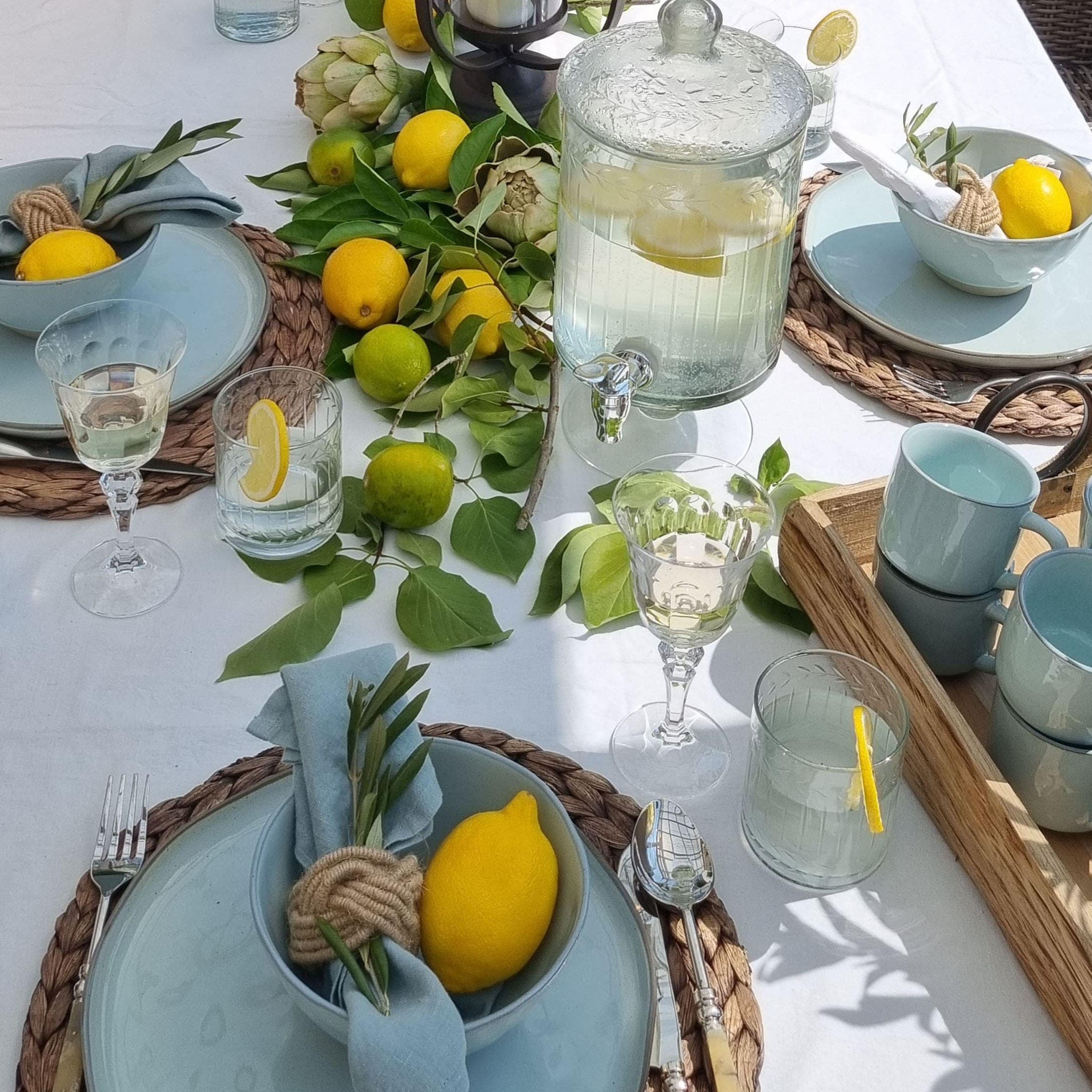 Table d'été avec vaisselle bleue, citrons et feuillage vert sur nappe blanche, décoration de table