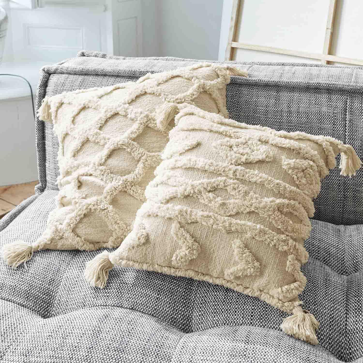 Coussins décoratifs beige en coton avec pompons sur canapé gris, texture et motifs tissés