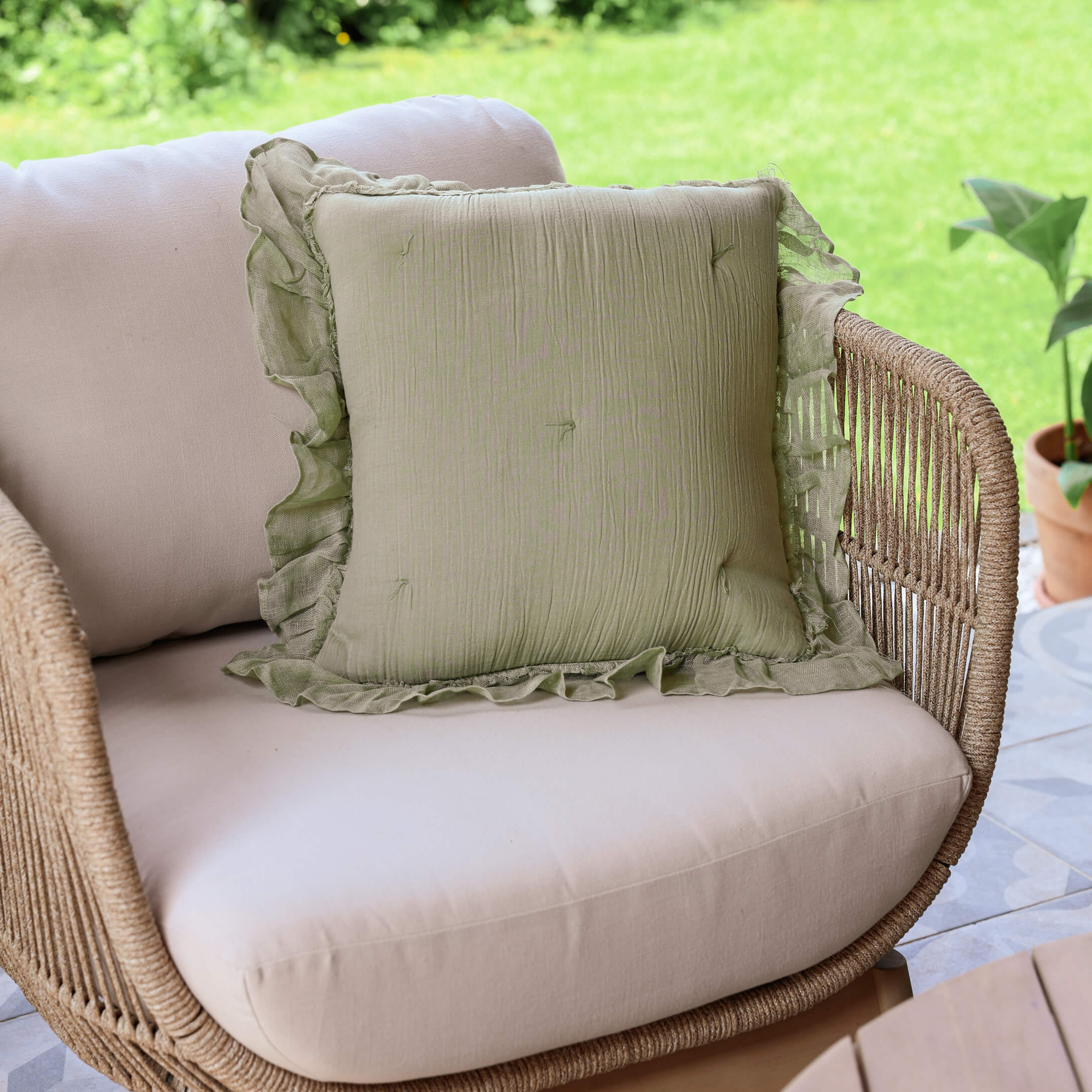 Coussin décoratif vert en lin avec volant sur canapé beige en rotin sur terrasse extérieure