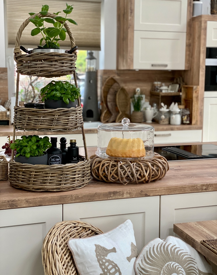 Présentoir à trois niveaux en osier avec plantes vertes et cloche en verre pour gâteau sur plan de travail en bois
