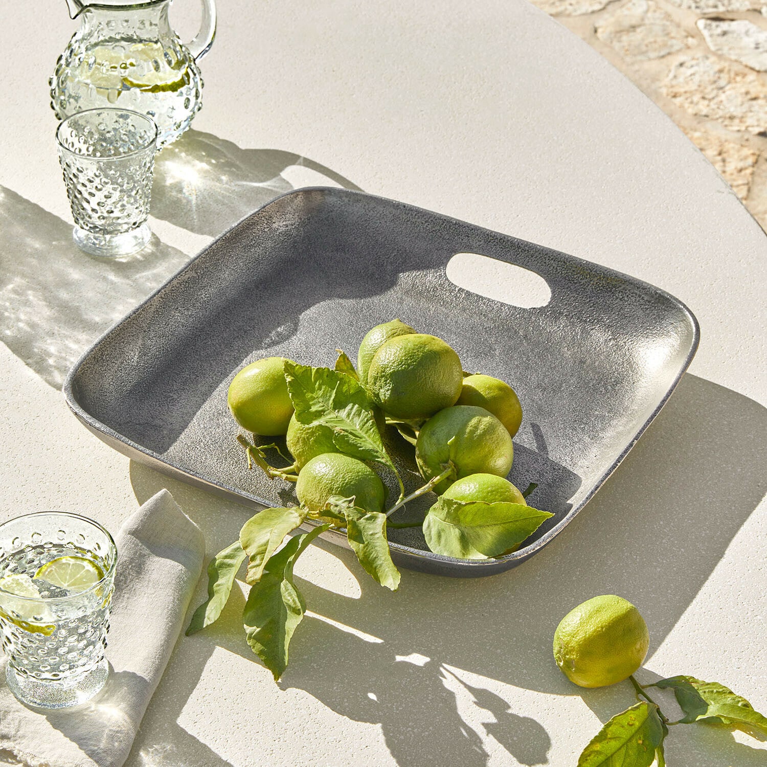 Plateau Tarevo Plateau carré en métal gris avec citrons verts sur une table claire, décoration de table estivale