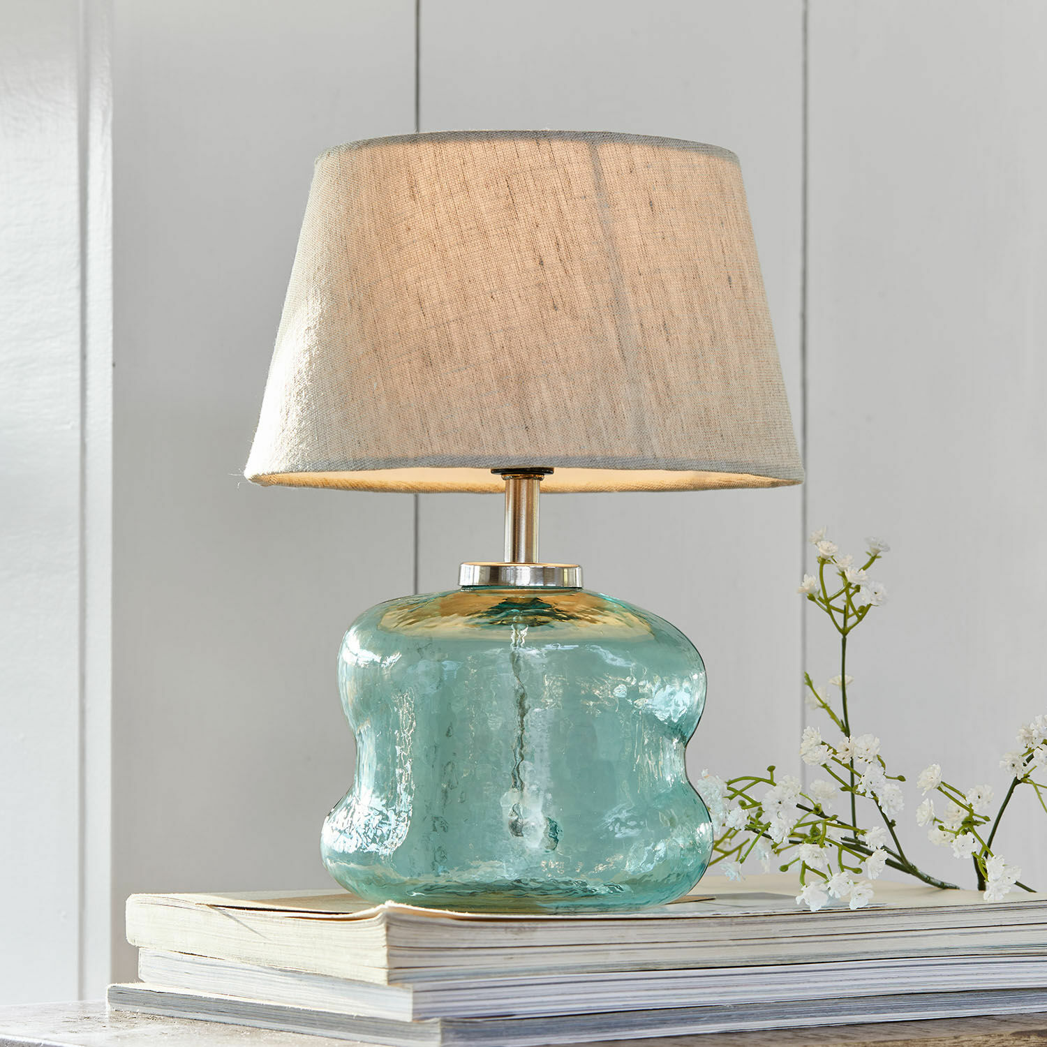 Lampe à poser Rufino Lampe de table en verre bleu avec abat-jour beige posée sur une pile de livres, décoration intérieure