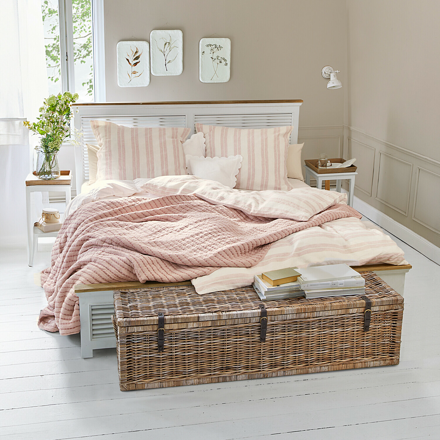 Lit Antje Chambre cosy avec lit à rayures roses claires et coffre en osier sur un sol blanc