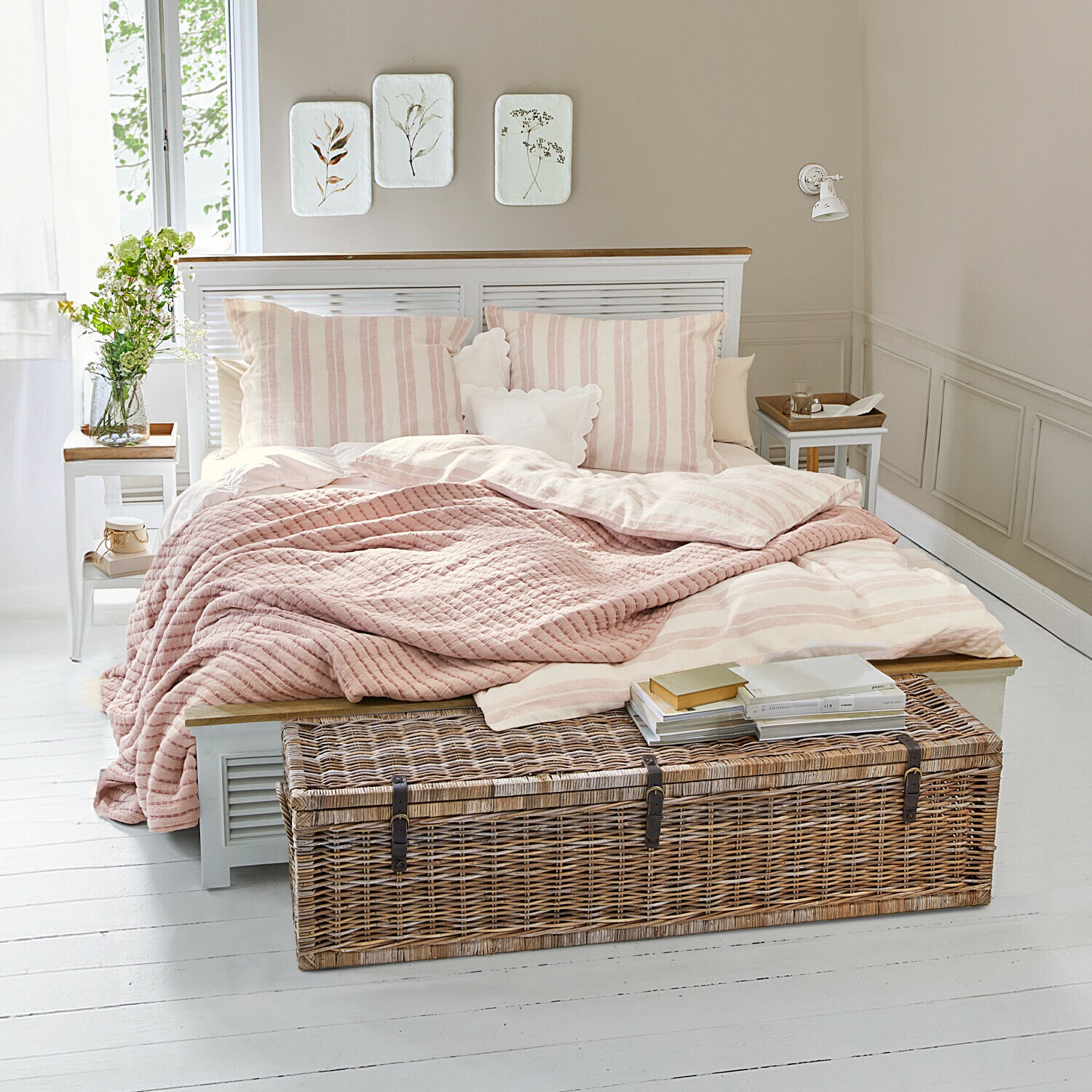 Lit Antje Chambre cosy avec lit à rayures roses claires et coffre en osier sur un sol blanc