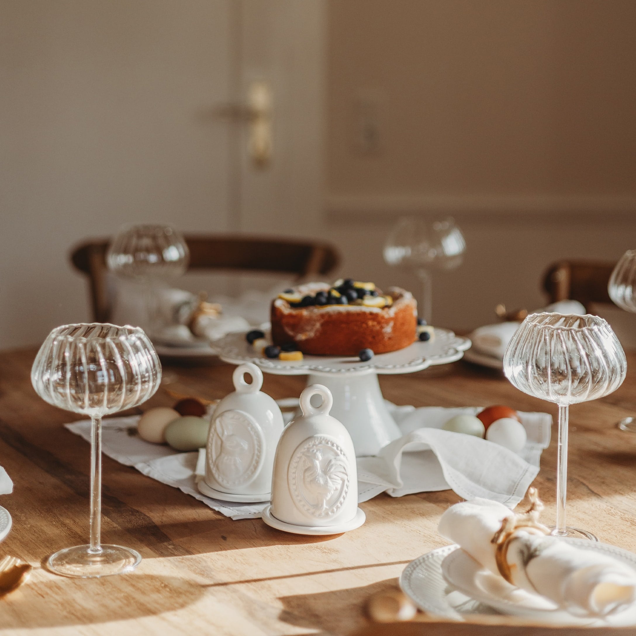 Clochettes décoratives en céramique blanche avec motif coq sur table en bois avec gâteau et verres