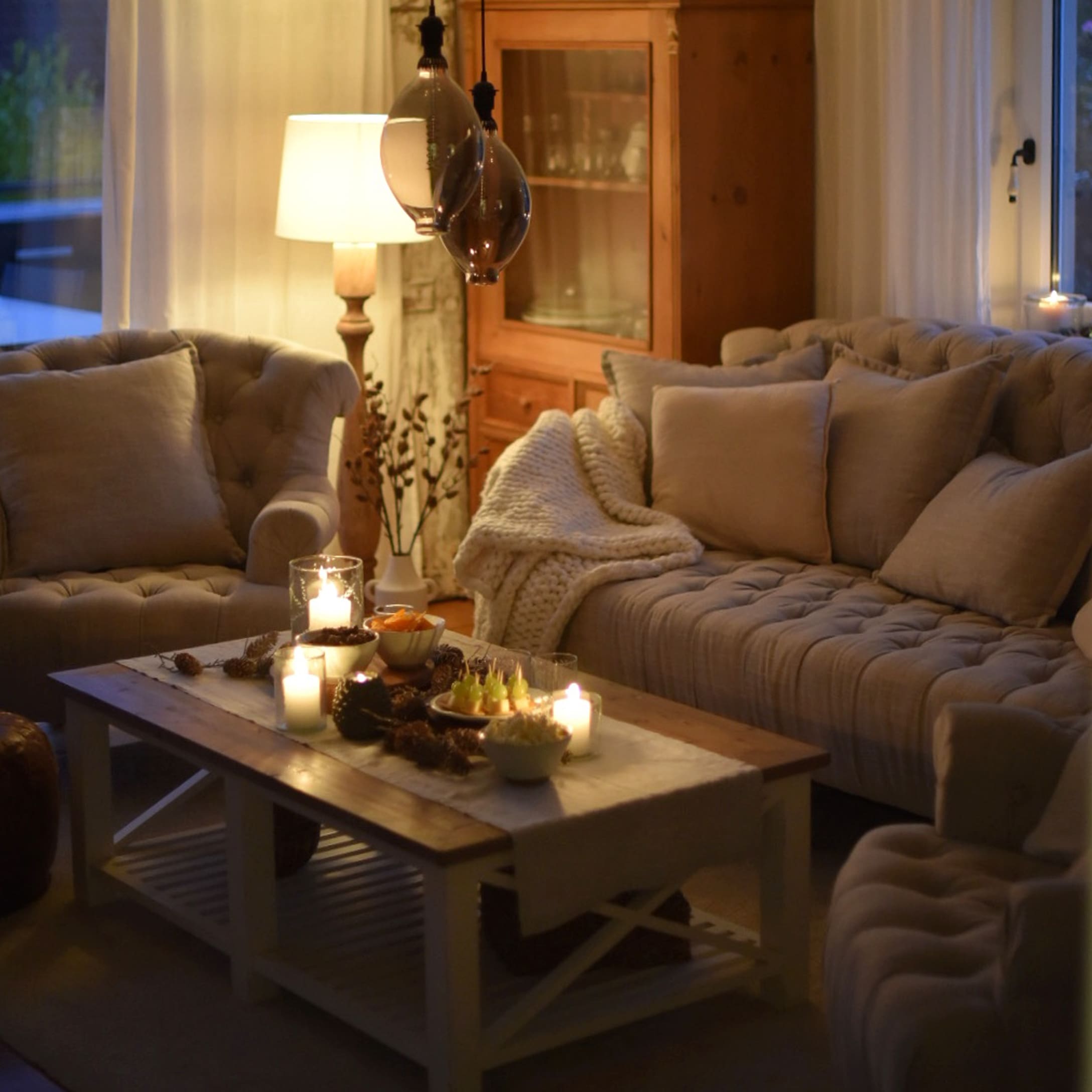 Salon chaleureux avec canapé beige, fauteuils et table basse en bois décorée de bougies et snacks