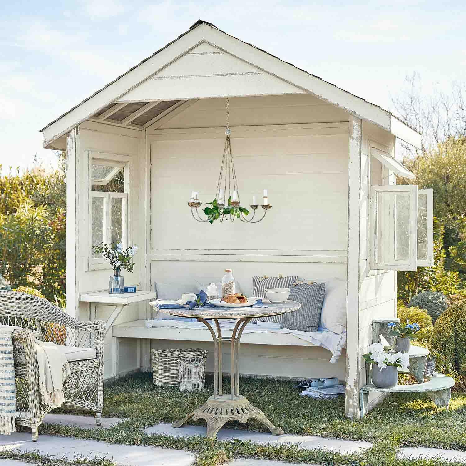 Kiosque de jardin en bois blanc avec fauteuil en osier et table ronde sur pelouse