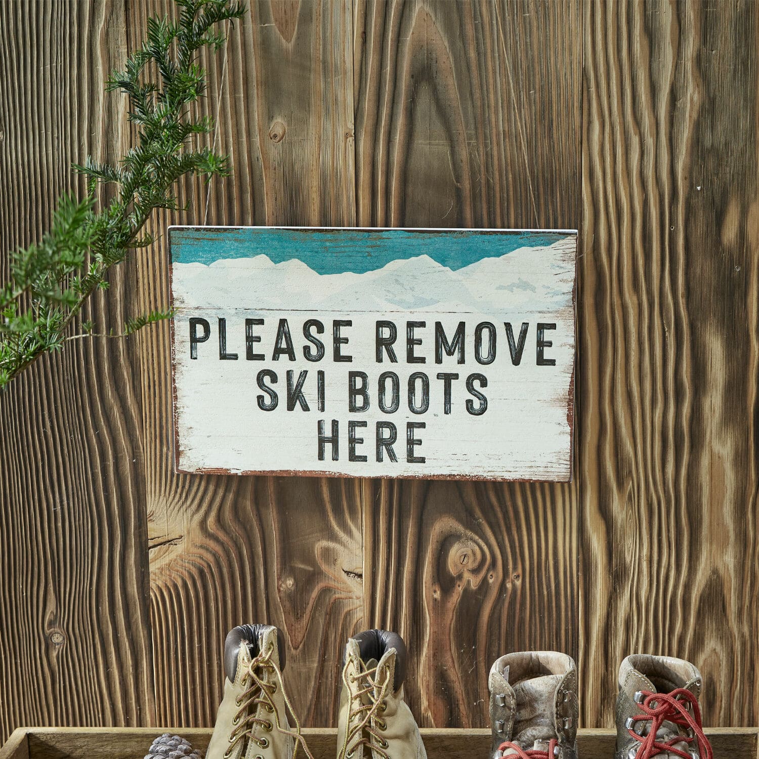 Tableau décoratif Uptonvale Panneau en bois indiquant de retirer les chaussures de ski avec des bottes de ski devant un mur en bois.