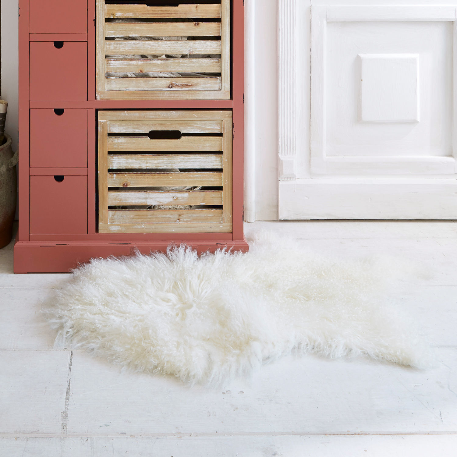 Peau d'agneau Gad Tapis blanc doux en laine naturelle posé sur un sol clair près d'une armoire rouge