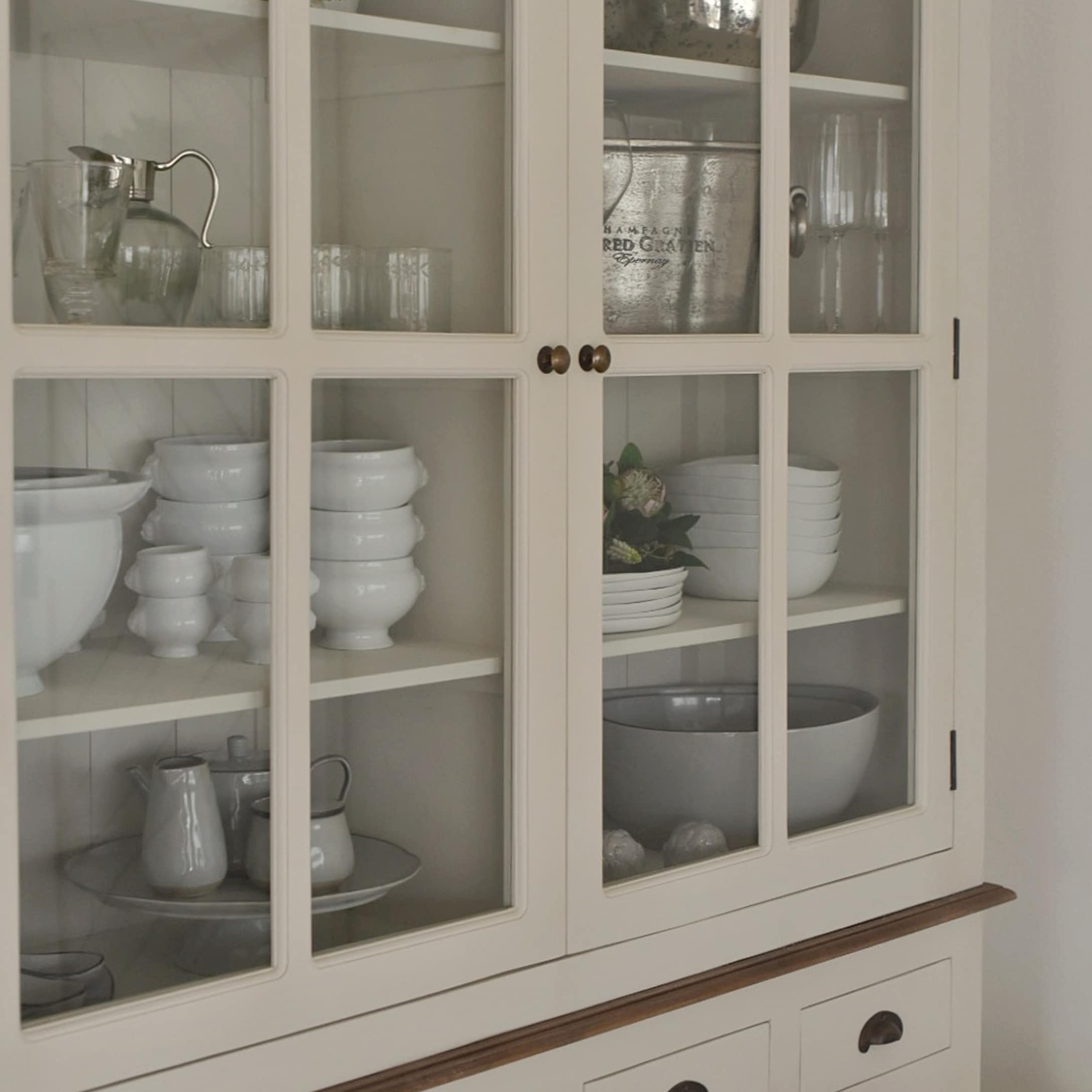 Vitrine en bois crème avec portes vitrées et vaisselle blanche à l'intérieur