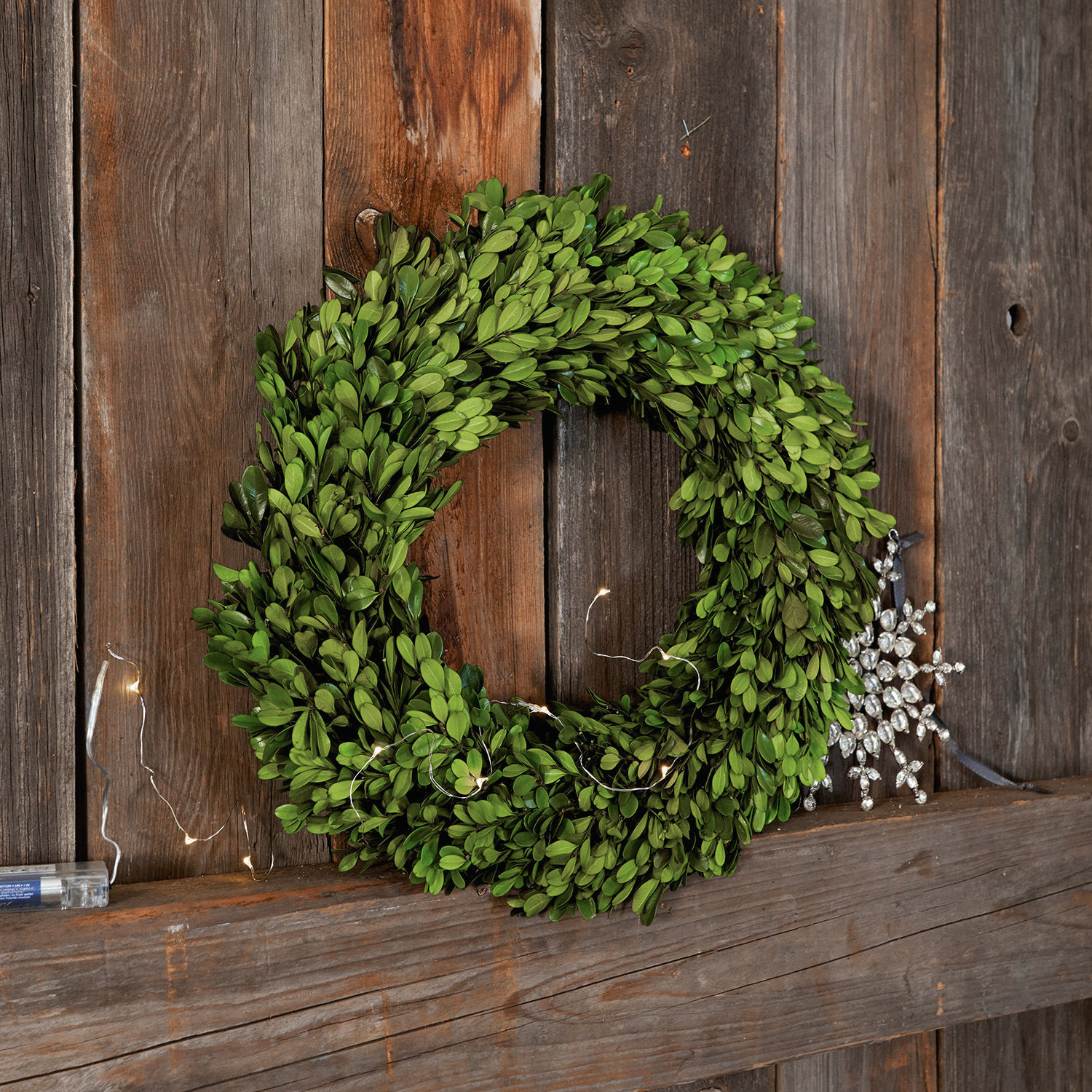 Couronne Myrcella Couronne verte en feuilles de buis sur fond en bois avec décoration flocon de neige et guirlande LED
