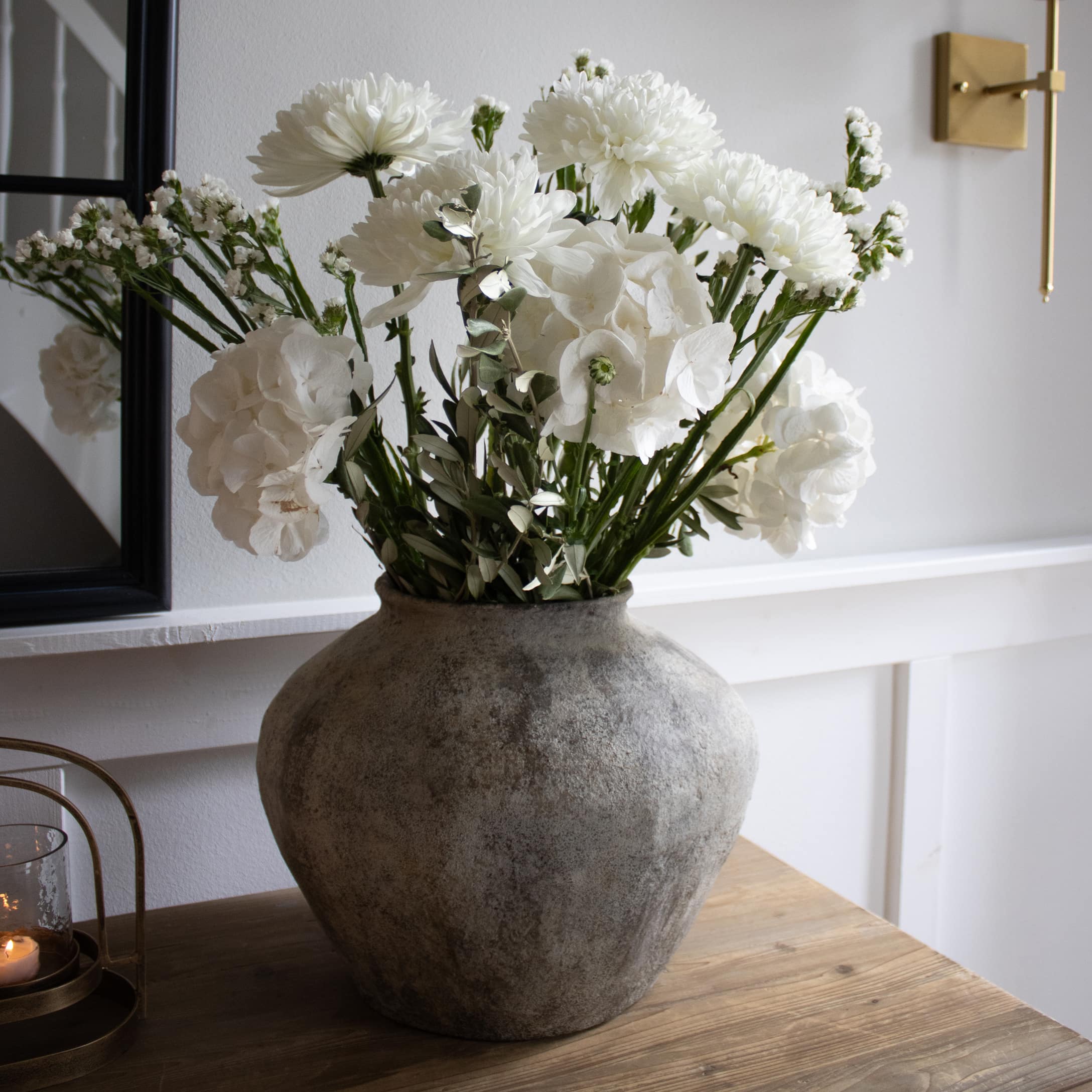 Grand vase gris avec fleurs blanches sur table en bois dans un intérieur lumineux