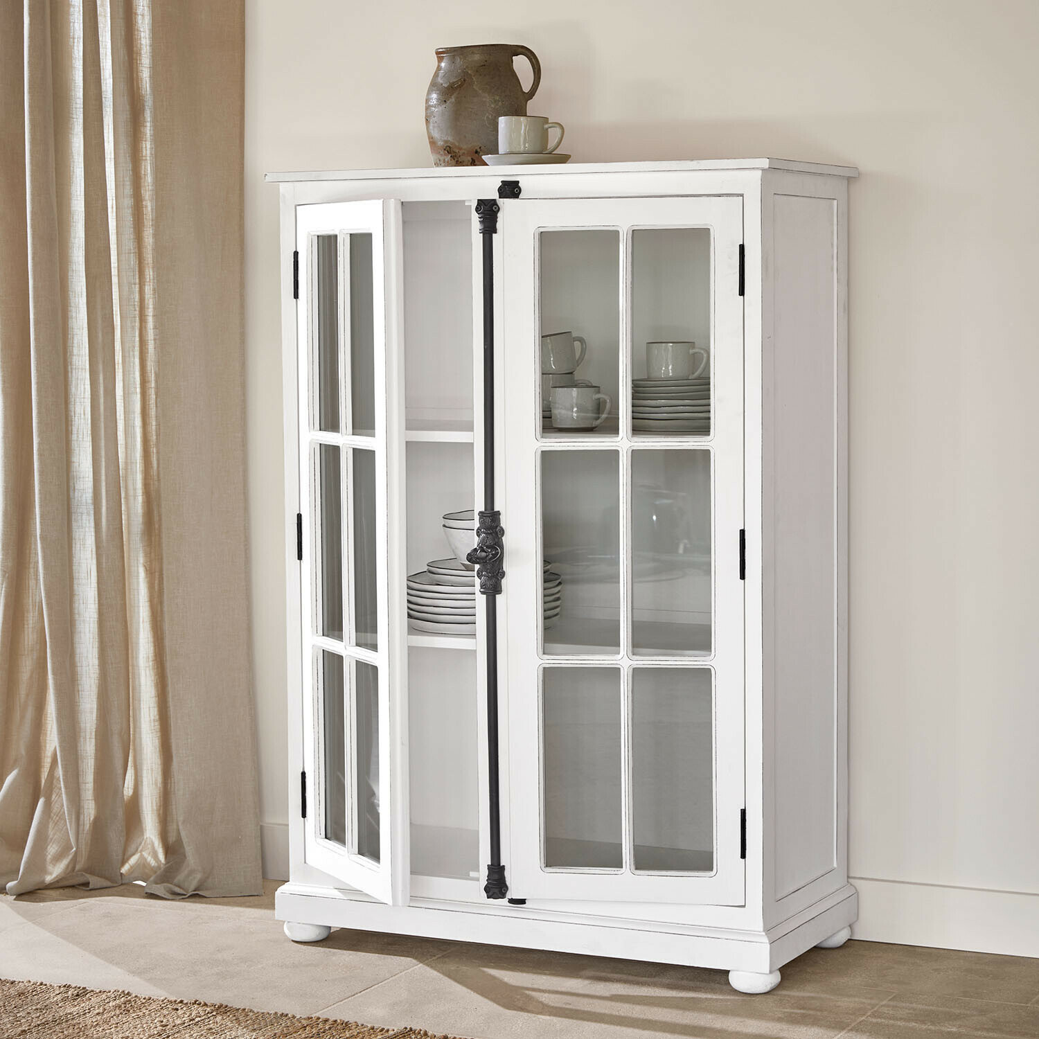 Vitrine Salivonne Vitrine en bois blanc avec portes vitrées et poignées en métal noir style vintage dans un intérieur clair