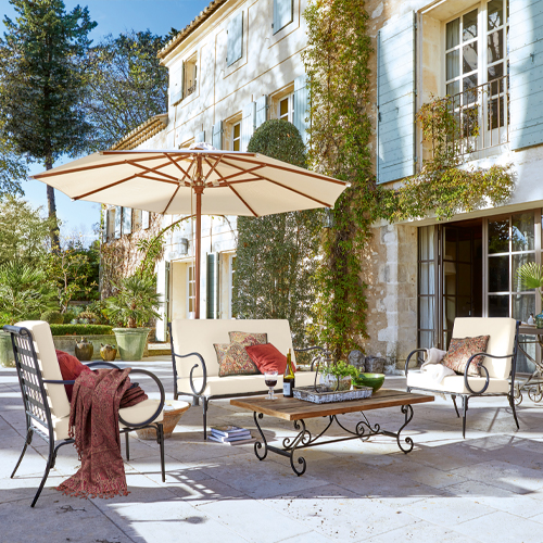 Ensemble de mobilier de jardin en métal avec coussins crème et parasol sur terrasse en pierre