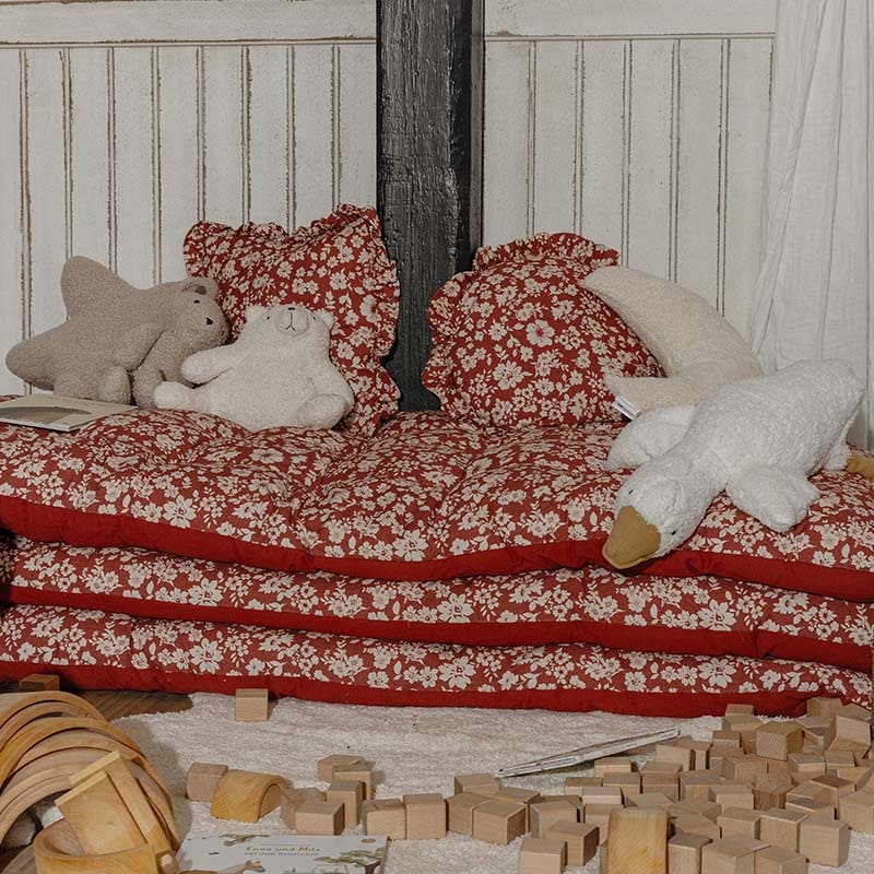 Coussins et matelas rouges à fleurs avec peluches sur un coin enfant entouré de blocs de bois pour jouer