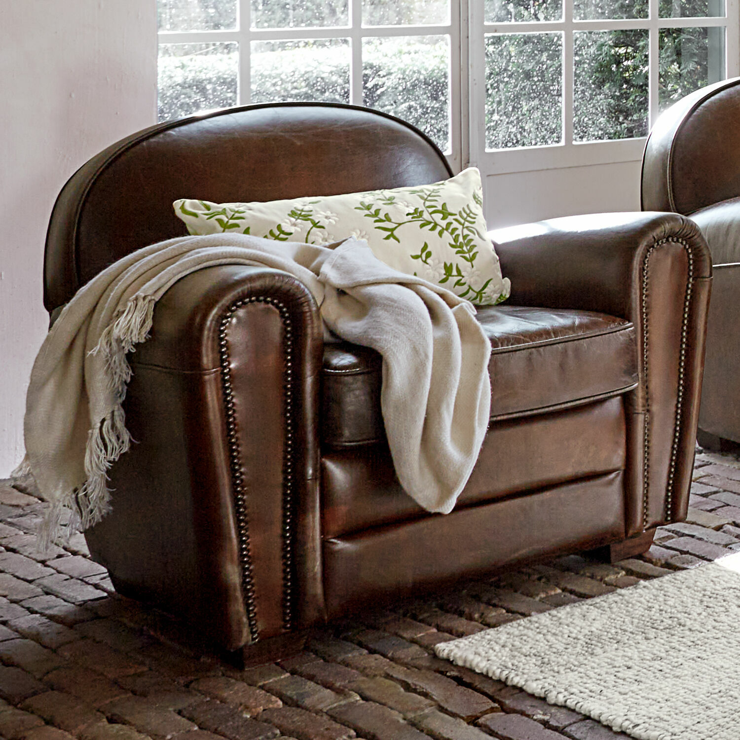 Fauteuil Venesque Fauteuil en cuir marron avec plaid blanc et coussin à motif vert dans une pièce lumineuse