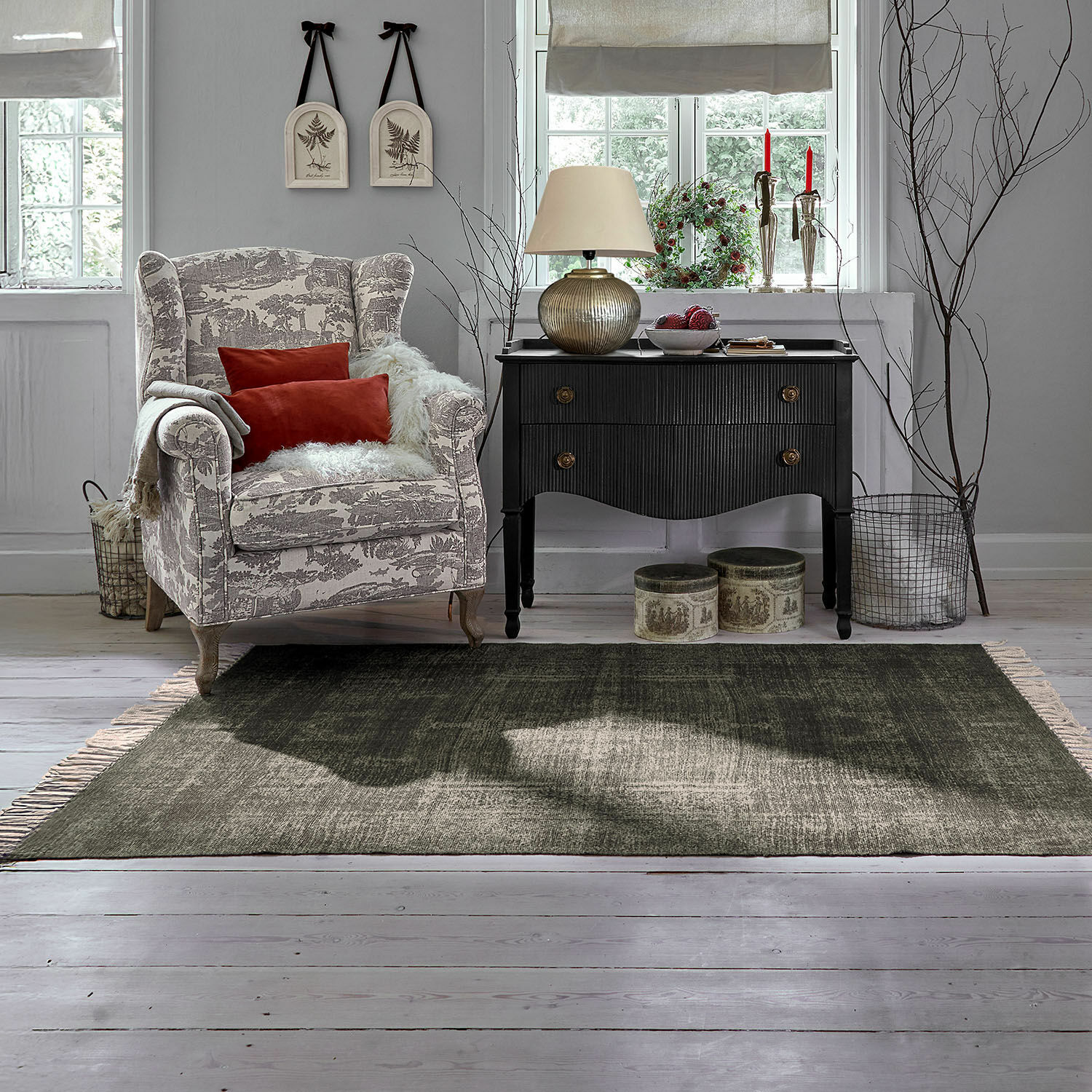 Tapis d’intérieur et d’extérieur Belaric Fauteuil beige à motifs gris avec coussins rouges et commode noire vintage dans un salon lumineux