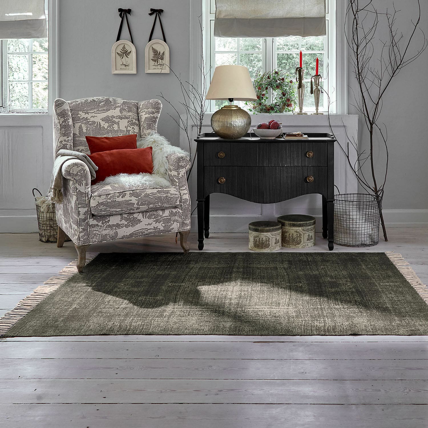 Tapis d’intérieur et d’extérieur Belaric Fauteuil beige à motifs gris avec coussins rouges et commode noire vintage dans un salon lumineux