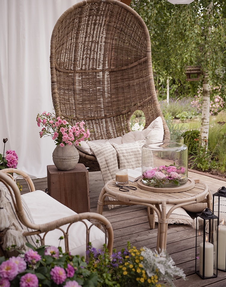 Coin détente avec fauteuil en osier et table basse sur terrasse décorée de fleurs et bougies