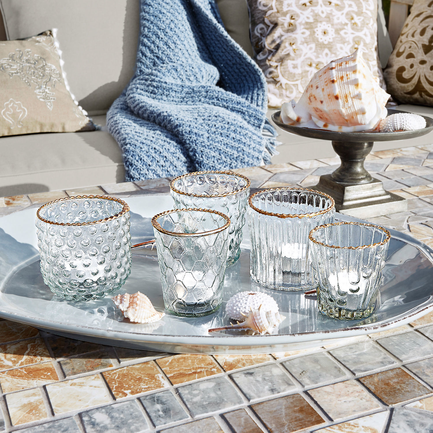 Lot de 5 photophores Jarnac Ensemble de cinq photophores en verre avec bord doré sur un plateau argenté posé sur une table en mosaïque