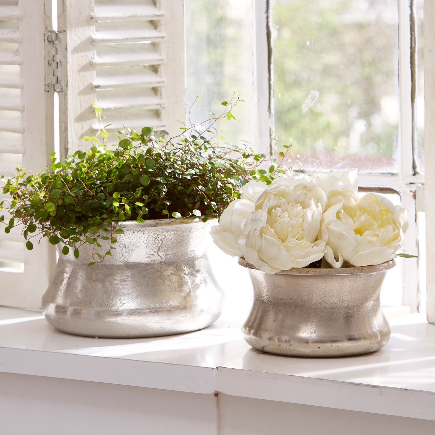 Lot de 2 vases Riona Deux pots en métal argenté sur un rebord de fenêtre avec plante verte et fleurs blanches décoratives