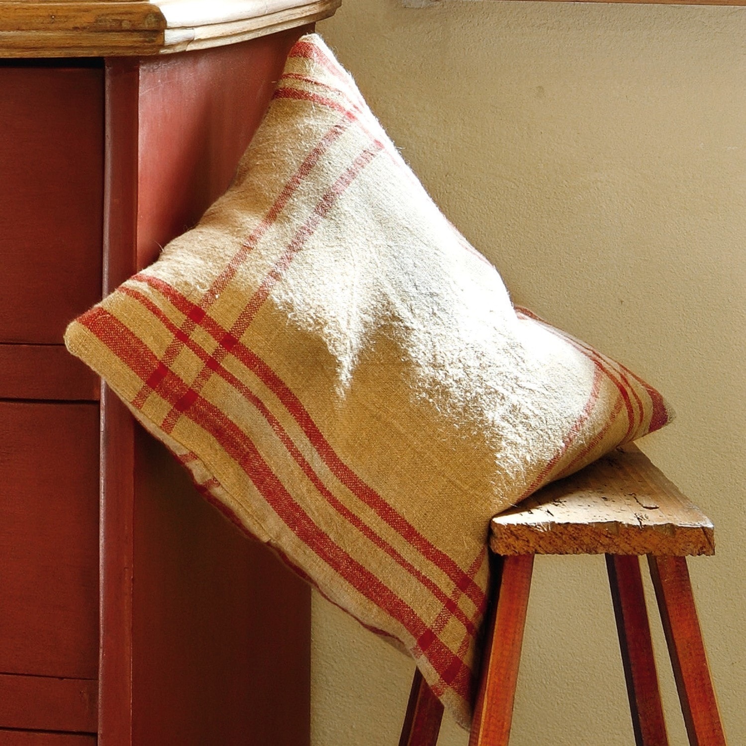 Housse de coussin Damian Coussin beige à motif rouge à carreaux posé sur un banc en bois, décoration intérieure