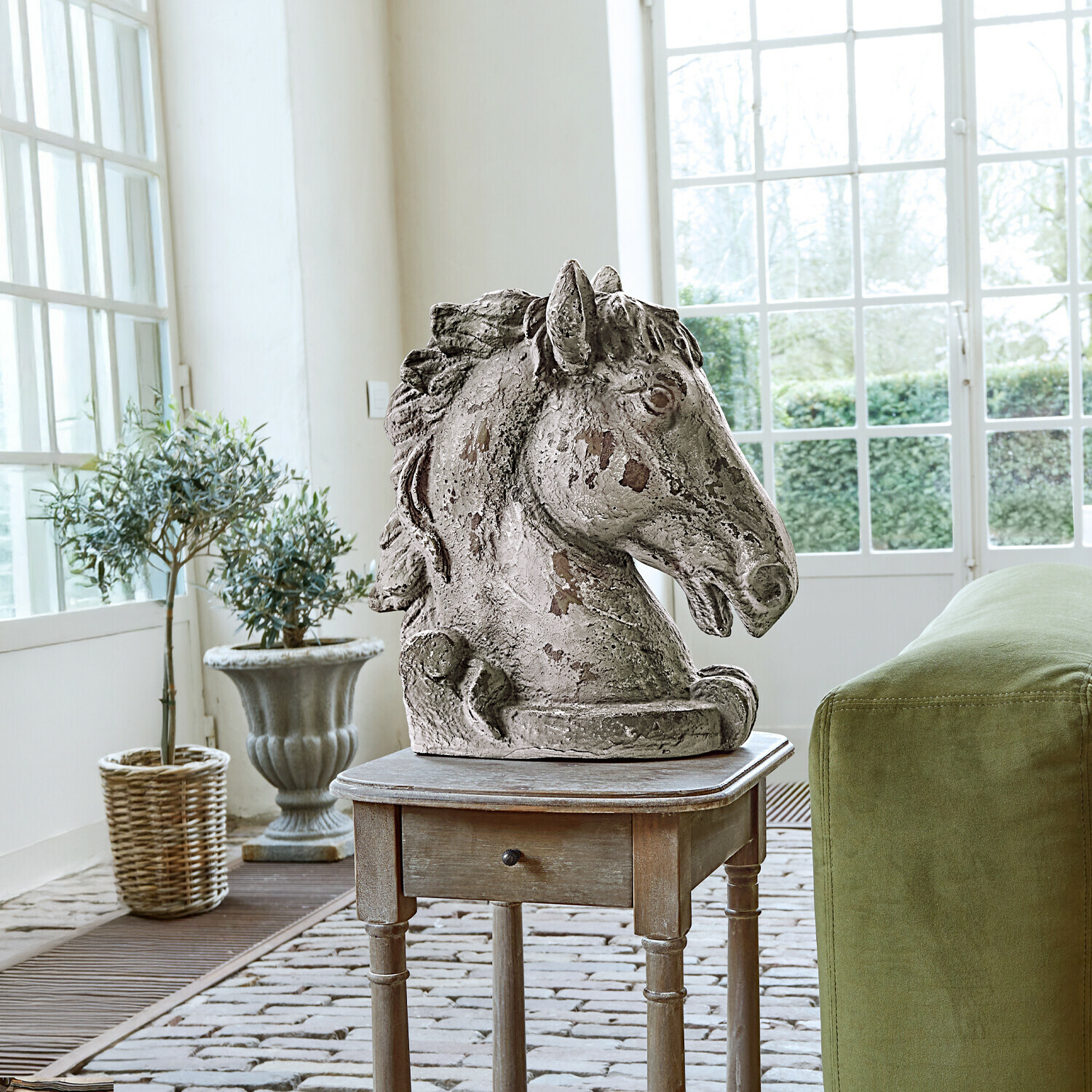 Cheval décoratif Ghenire Sculpture tête de cheval en pierre vieillie sur table en bois à côté d'un canapé vert avec coussin brodé