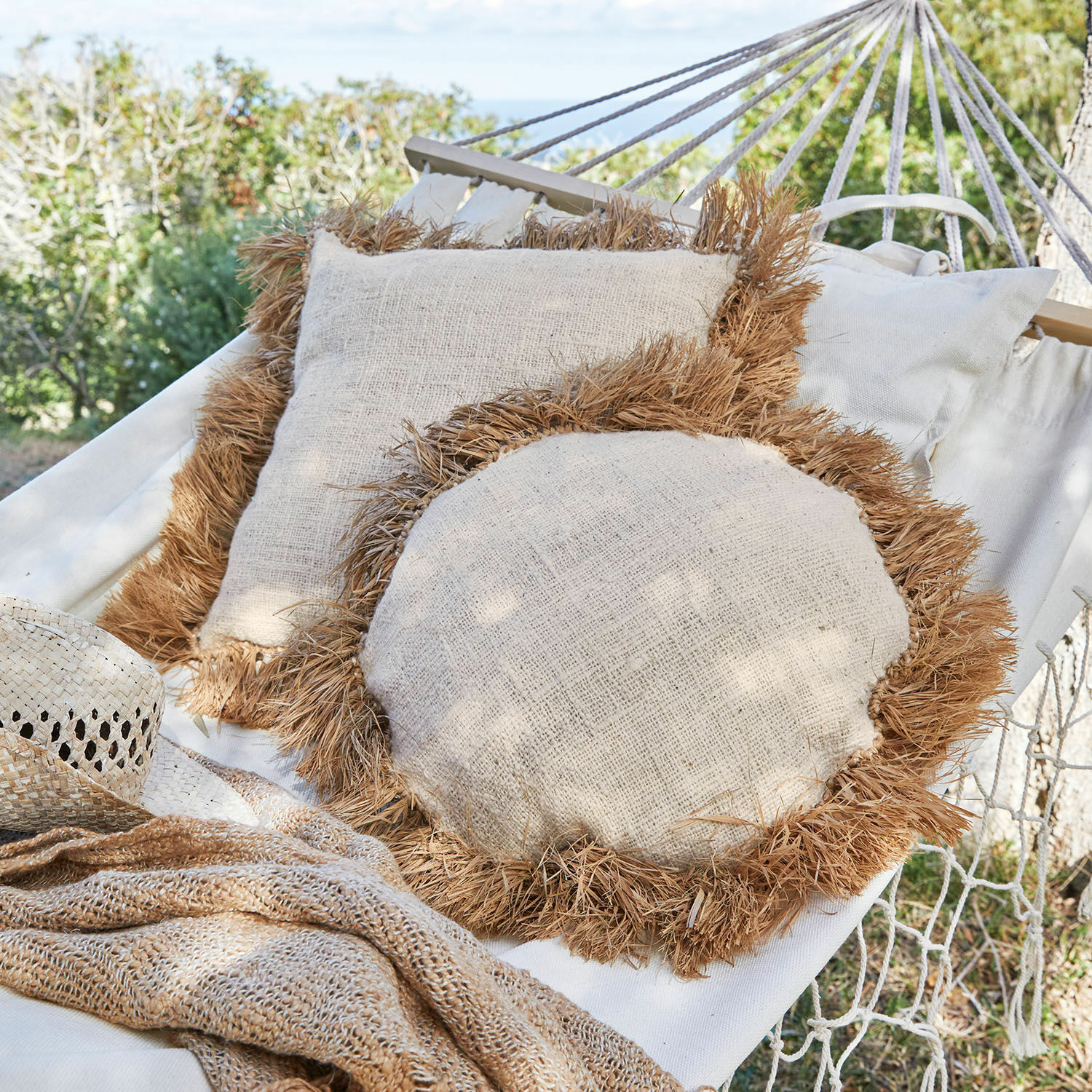 Lot de 2 coussins Adavale Coussins beiges en lin naturel avec franges brunes posés sur un hamac en extérieur, déco jardin