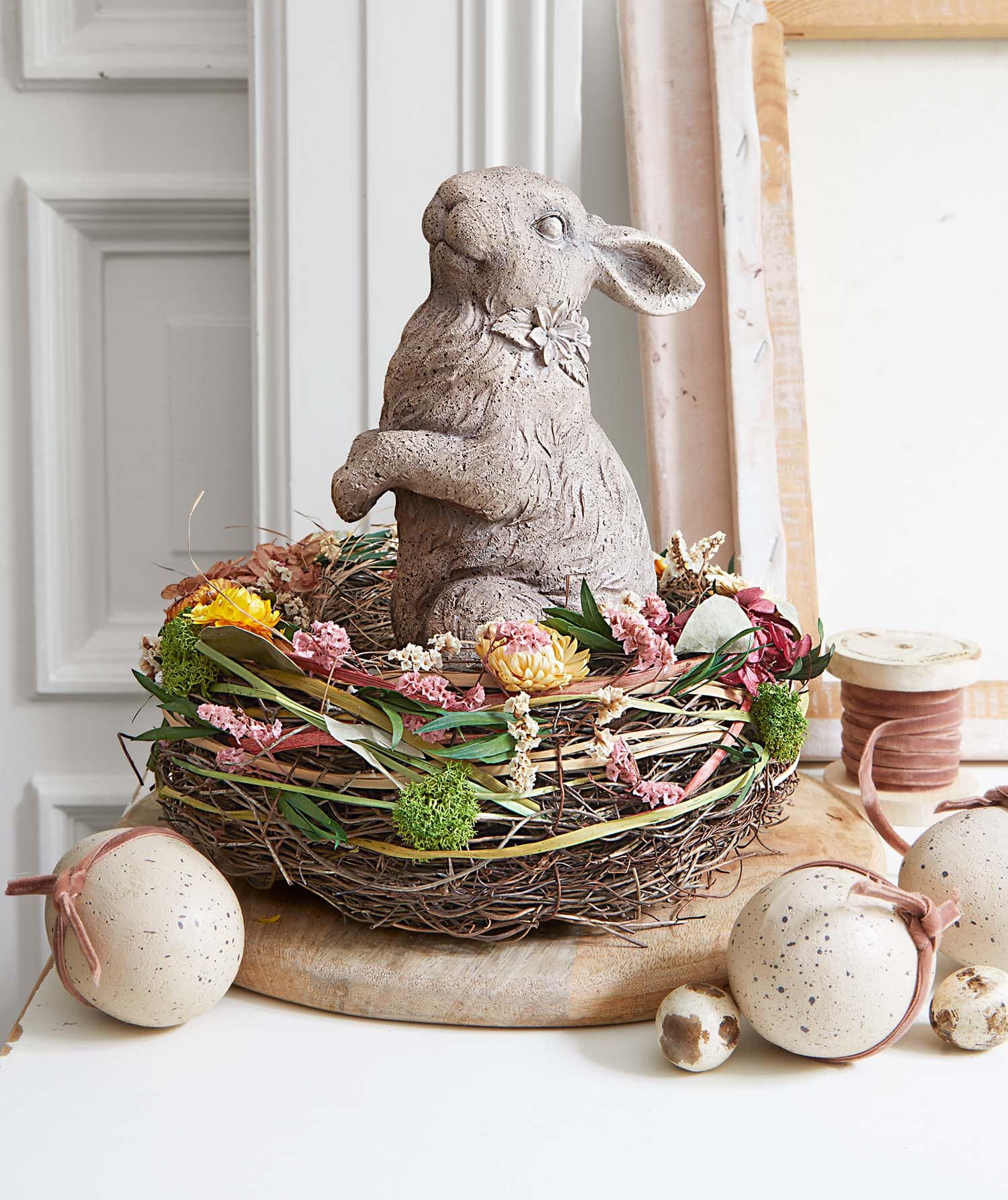 Lapin décoratif en béton dans un nid avec fleurs séchées et œufs décoratifs pour Pâques