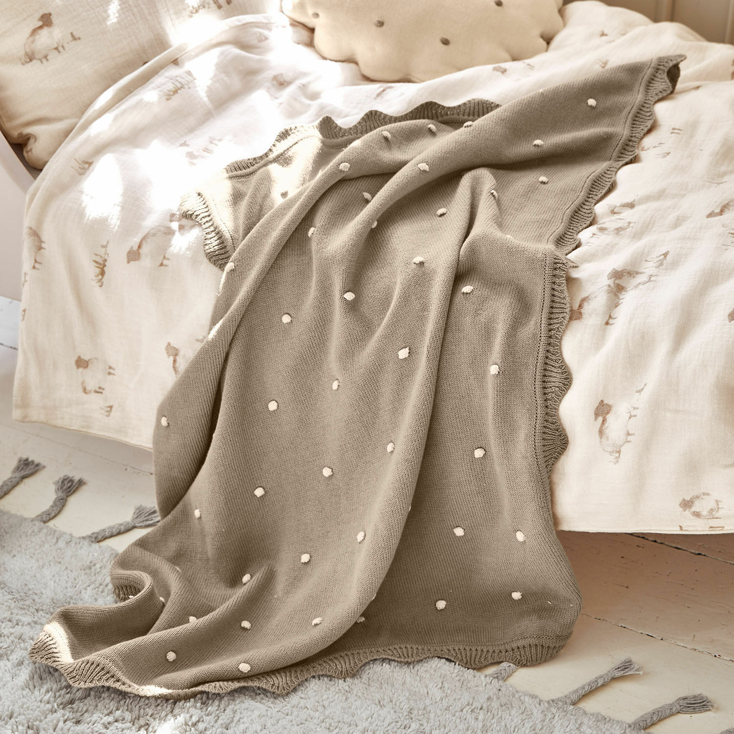 Plaid Saphie Plaid tricoté beige à pois blancs sur lit avec linge de lit clair, couverture douce et décorative