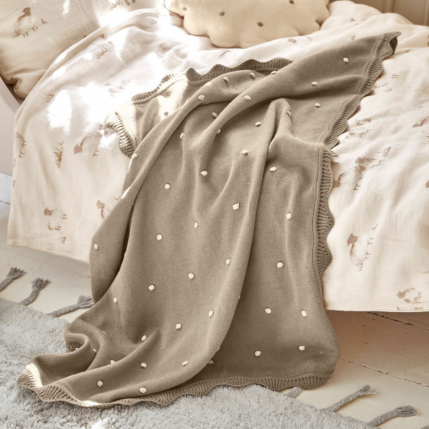 Plaid Saphie Plaid tricoté beige à pois blancs sur lit avec linge de lit clair, couverture douce et décorative