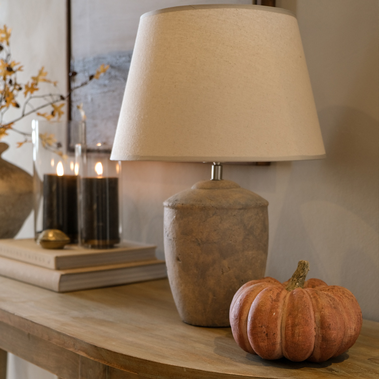 Lampe de table avec abat-jour beige et base en pierre sur une table en bois avec décoration citrouille