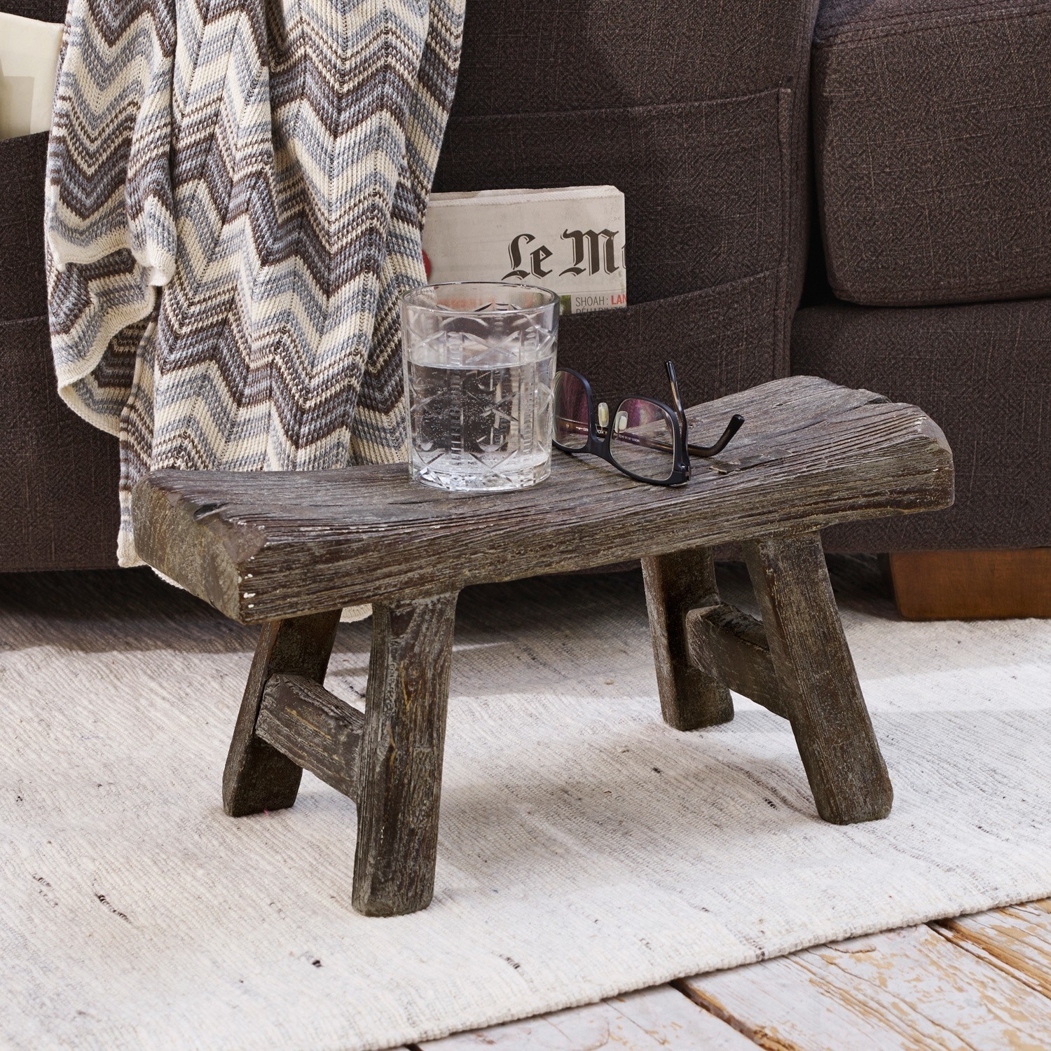 Tabouret Cadoc Table basse rustique en bois foncé sur tapis clair près d'un canapé avec une couverture à chevrons