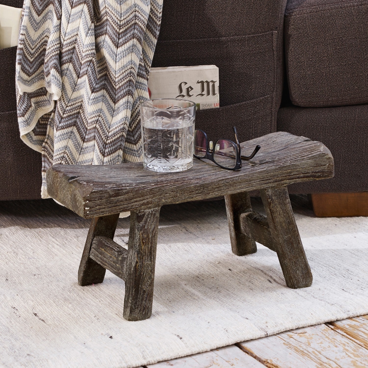 Tabouret Cadoc Table basse rustique en bois foncé sur tapis clair près d'un canapé avec une couverture à chevrons