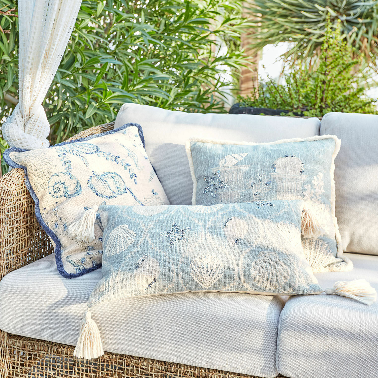 Lot de 3 housses de coussins Calerand Ensemble de coussins décoratifs bleu et beige avec motifs coquillages et étoiles de mer sur canapé en rotin