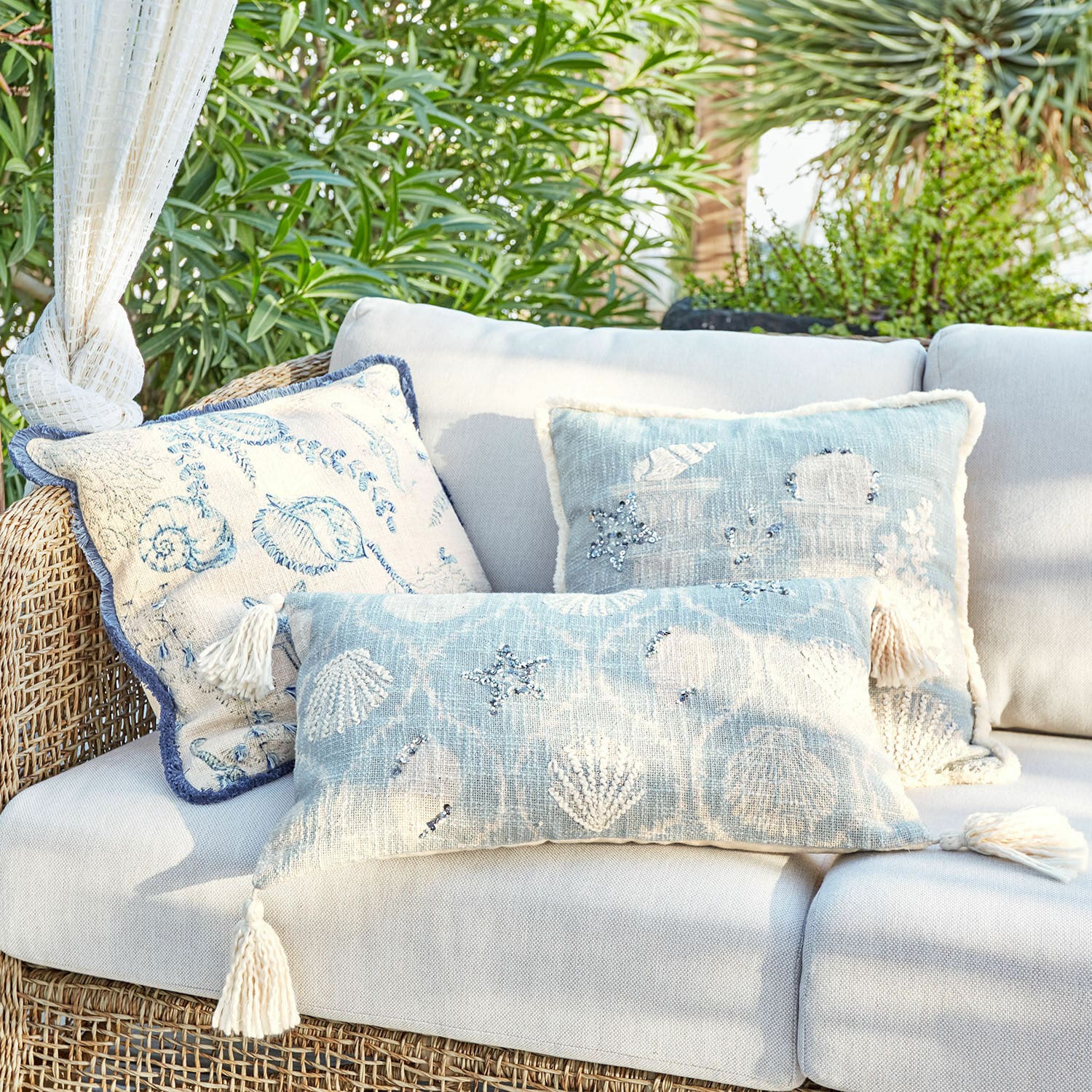 Lot de 3 housses de coussins Calerand Ensemble de coussins décoratifs bleu et beige avec motifs coquillages et étoiles de mer sur canapé en rotin