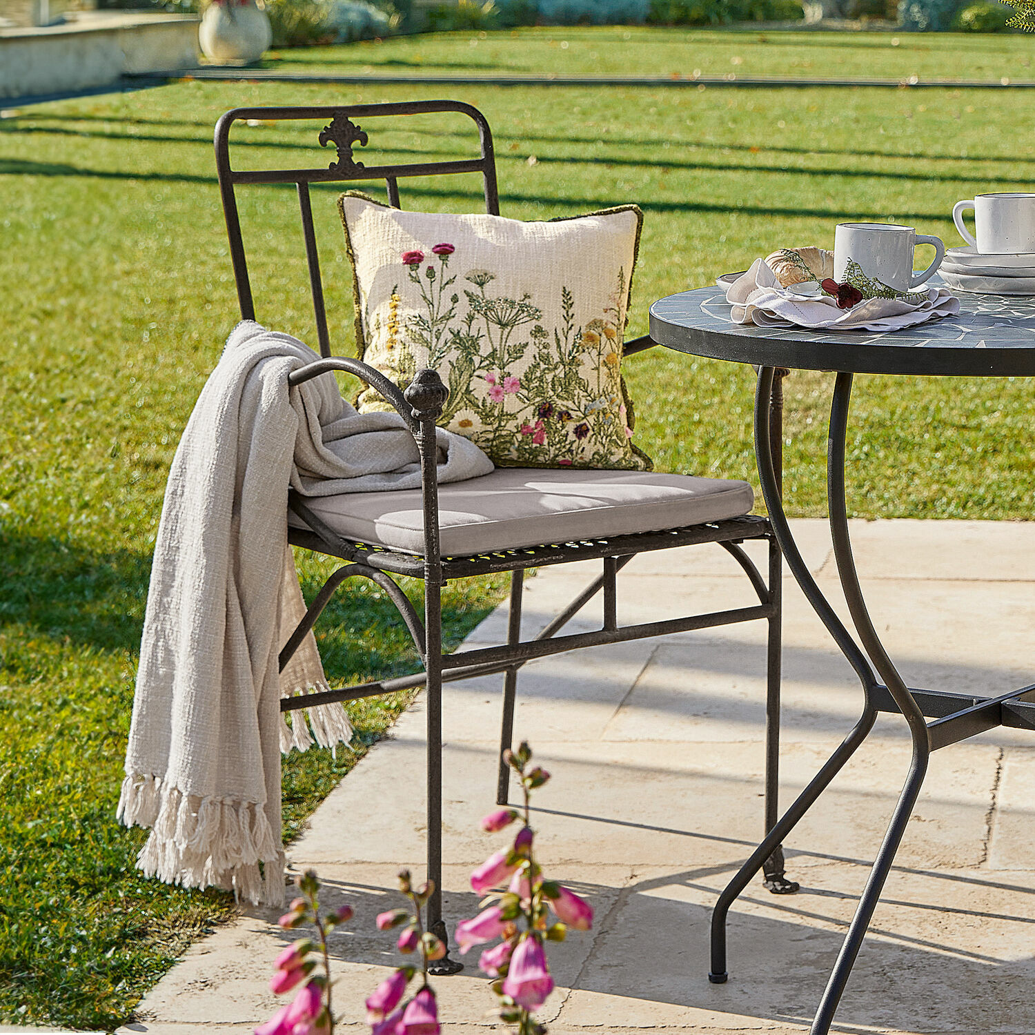 Chaise Maidis Fauteuil de jardin en métal noir avec coussin clair et coussin décoratif à motif floral sur terrasse ensoleillée