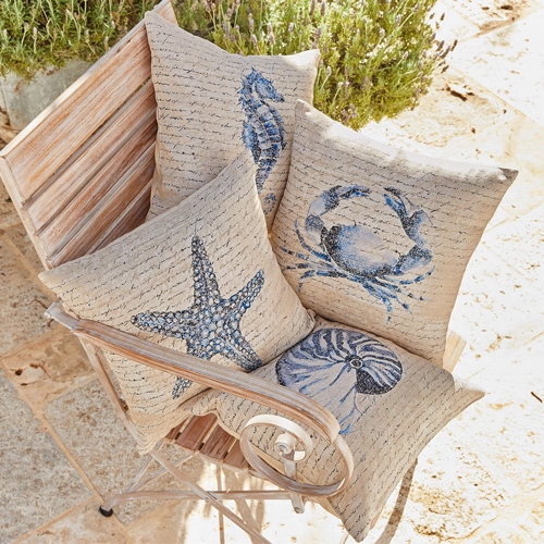 Quatre coussins beiges avec motifs marins et texte, posés sur une chaise en bois d'extérieur