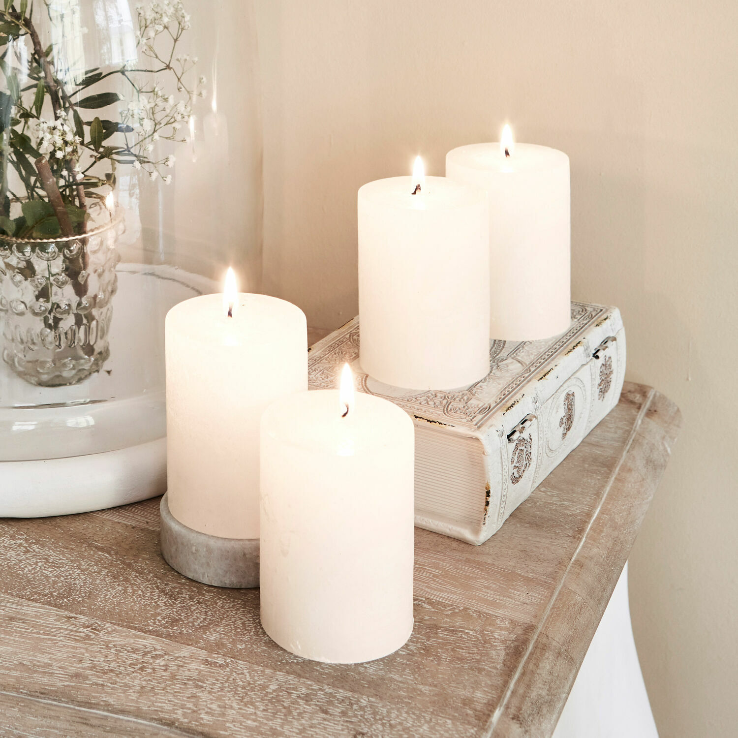 Lot de 4 bougies Virrans Quatre bougies blanches décoratives sur une table en bois avec un livre orné et un vase en verre