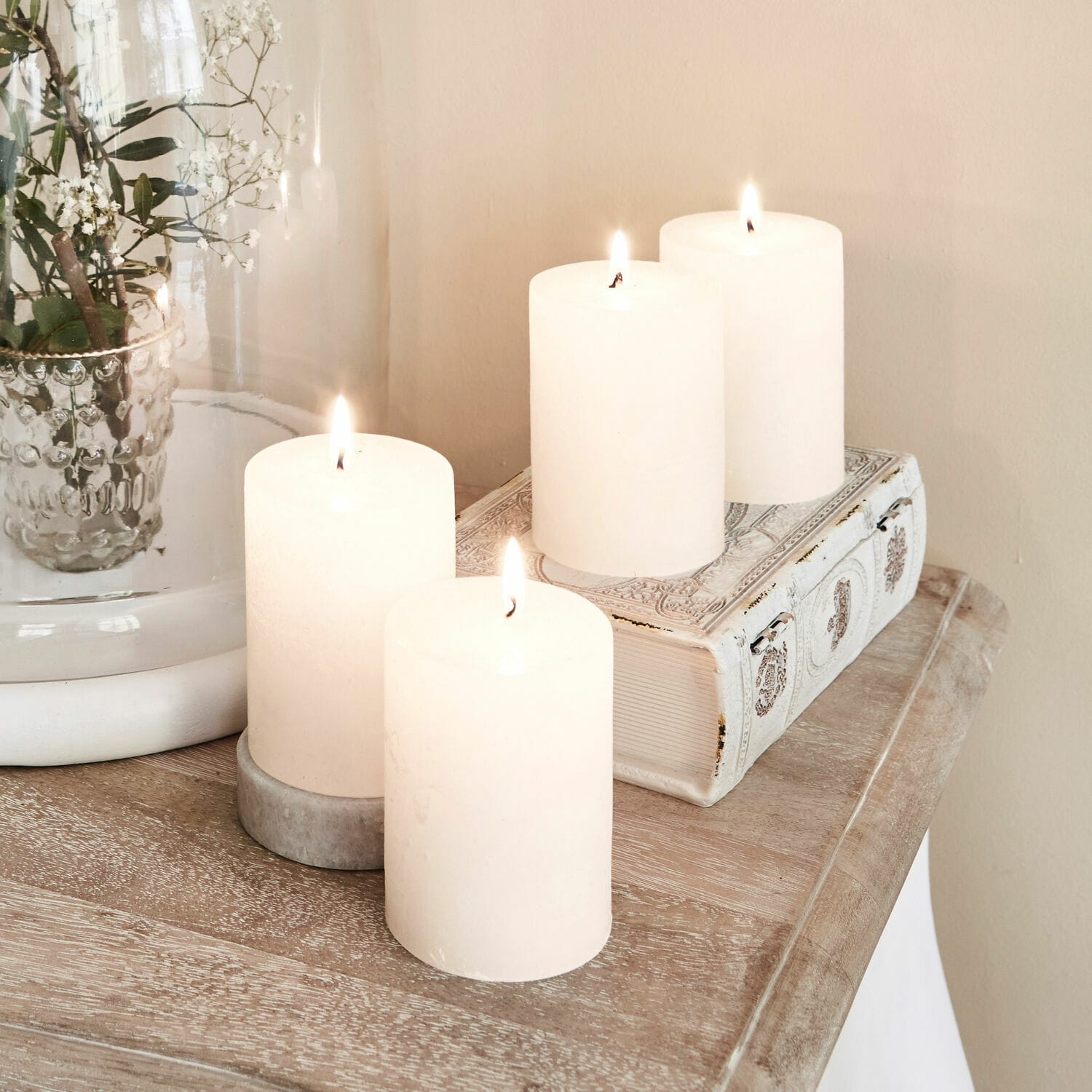 Lot de 4 bougies Virrans Quatre bougies blanches décoratives sur une table en bois avec un livre orné et un vase en verre