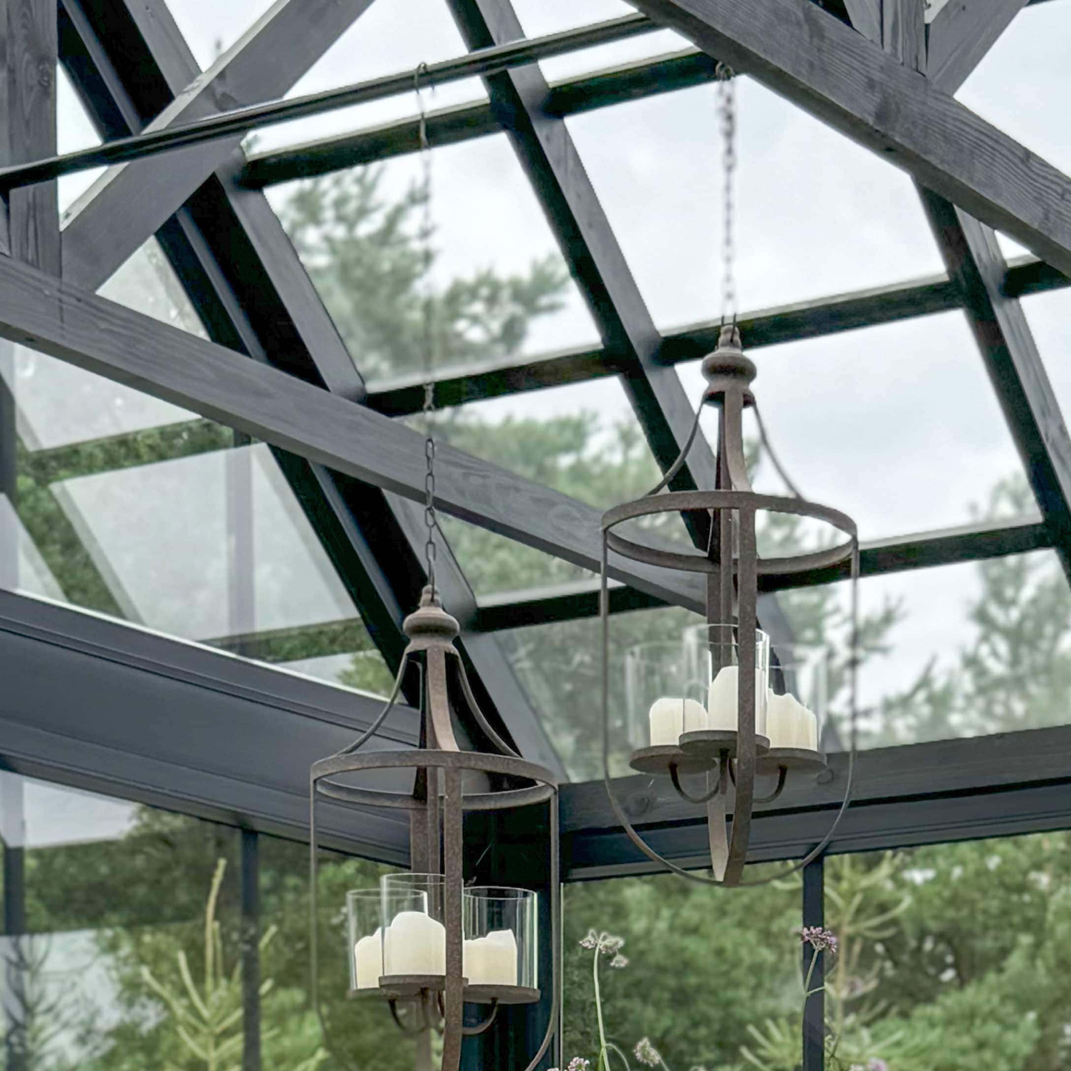 Lanterne suspendue en métal rouillé avec bougies blanches dans des protections en verre dans une serre