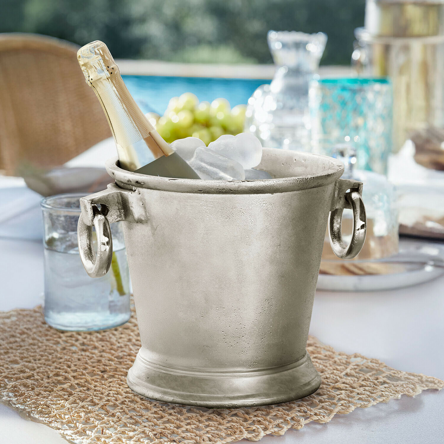 Seau à glace Cressford Seau à glace en métal argenté avec bouteille de champagne et glaçons sur table extérieure