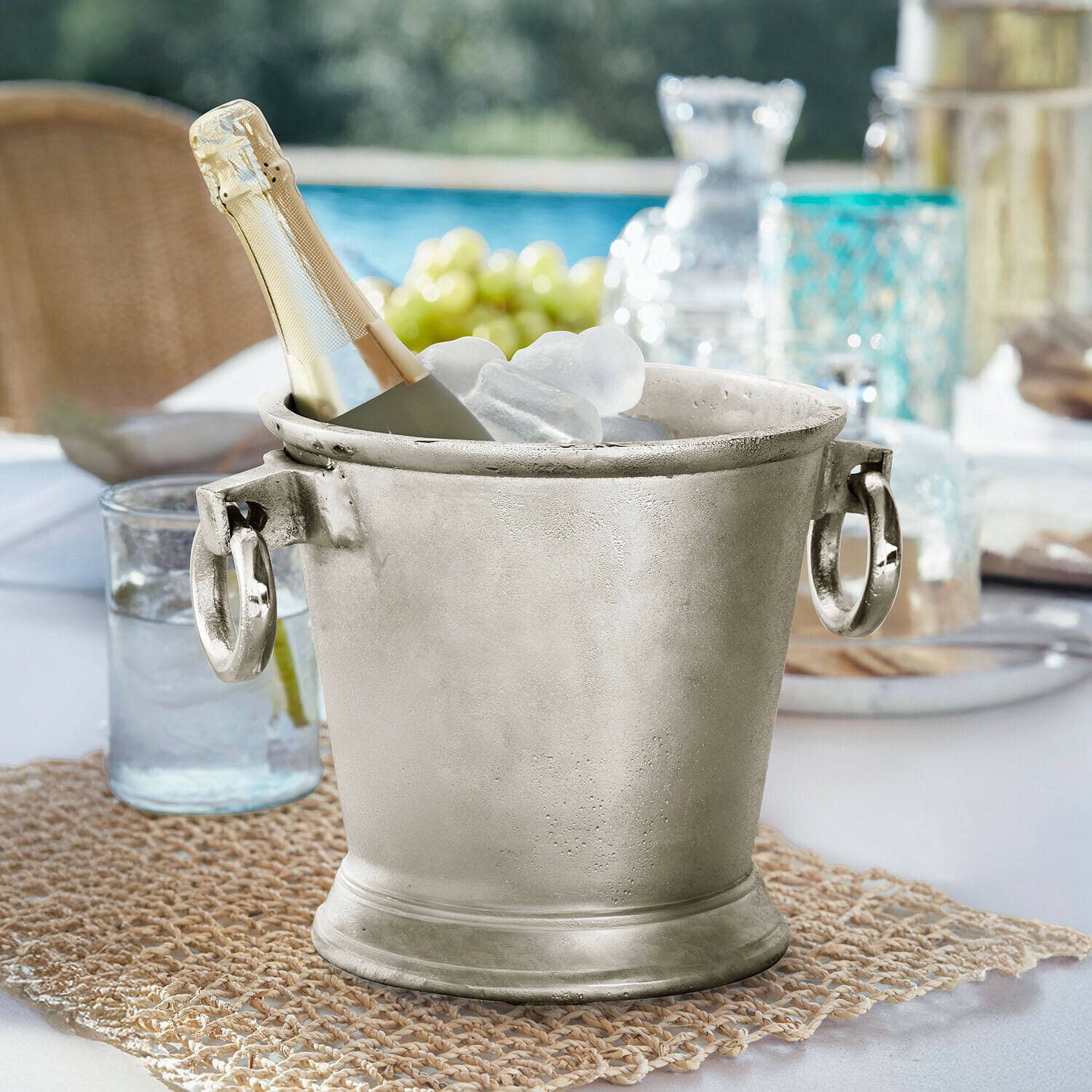 Seau à glace Cressford Seau à glace en métal argenté avec bouteille de champagne et glaçons sur table extérieure