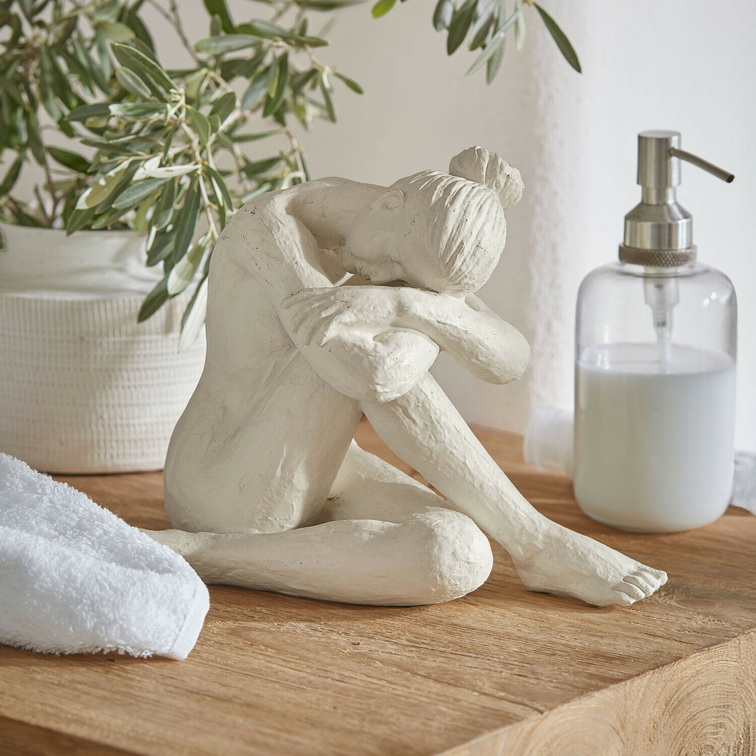 figurine Savigné Sculpture blanche d'une femme assise, tête posée sur les genoux, sur un plateau en bois dans une salle de bain