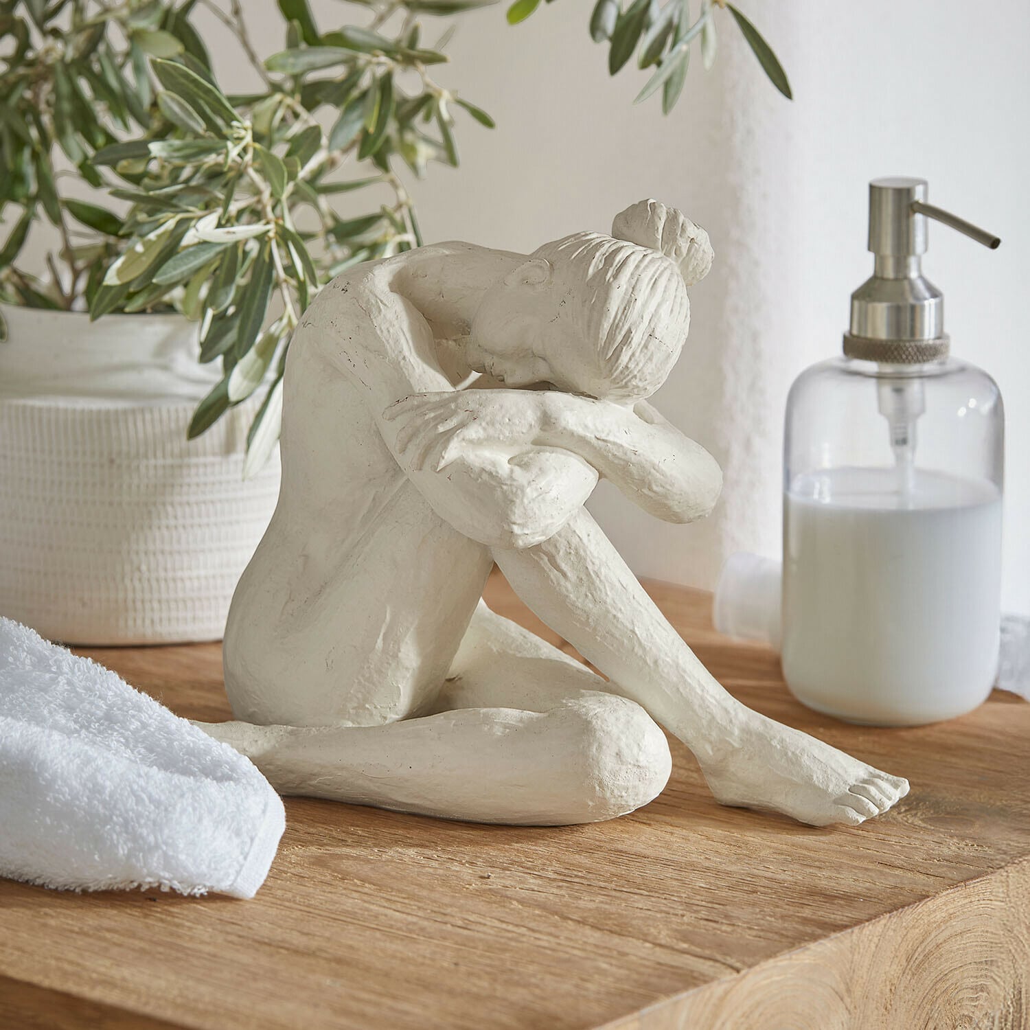 figurine Savigné Sculpture blanche d'une femme assise, tête posée sur les genoux, sur un plateau en bois dans une salle de bain